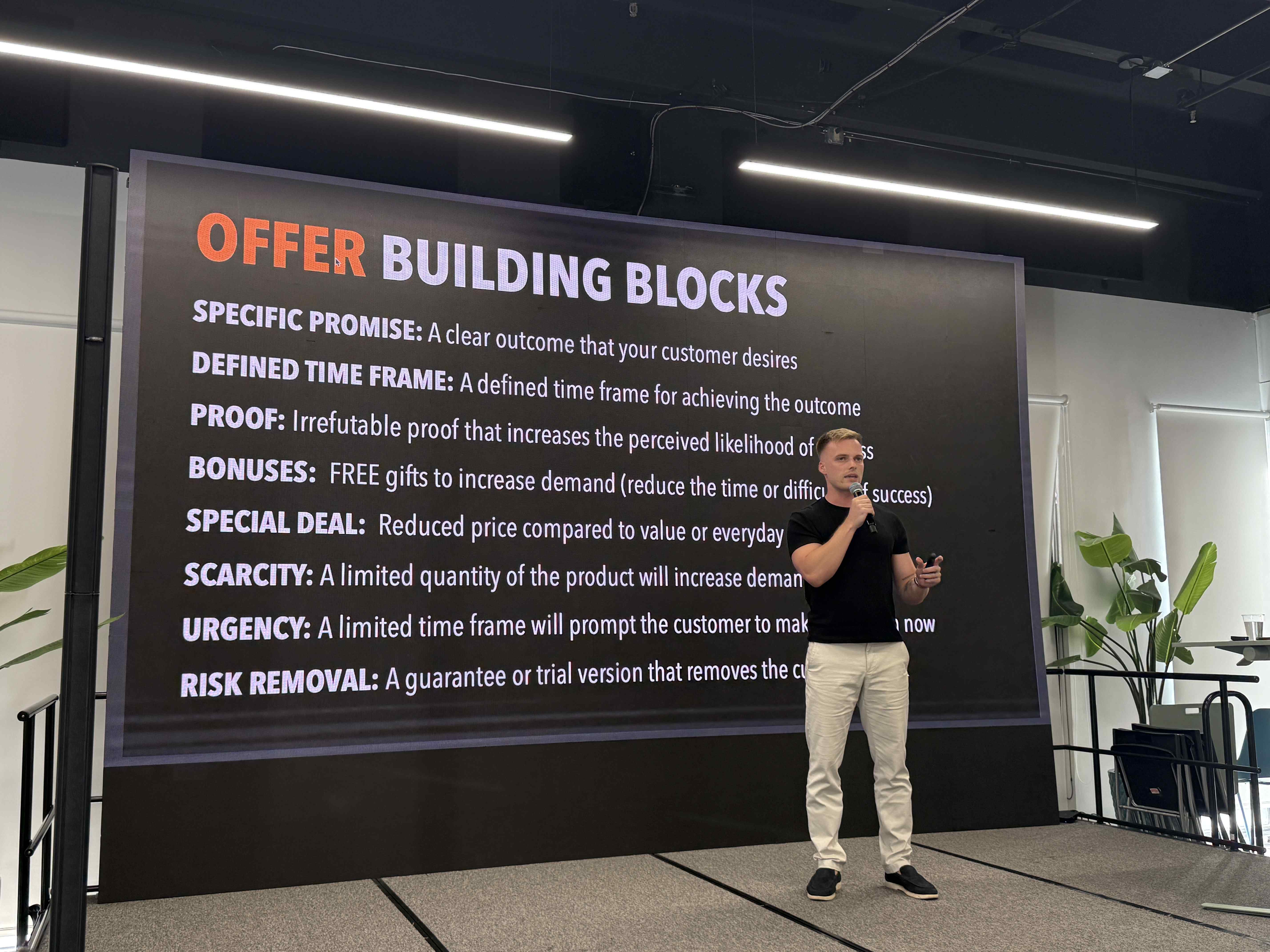 Přednášející s mikrofonem před slidem OFFER BUILDING BLOCKS na konferenčním pódiu.