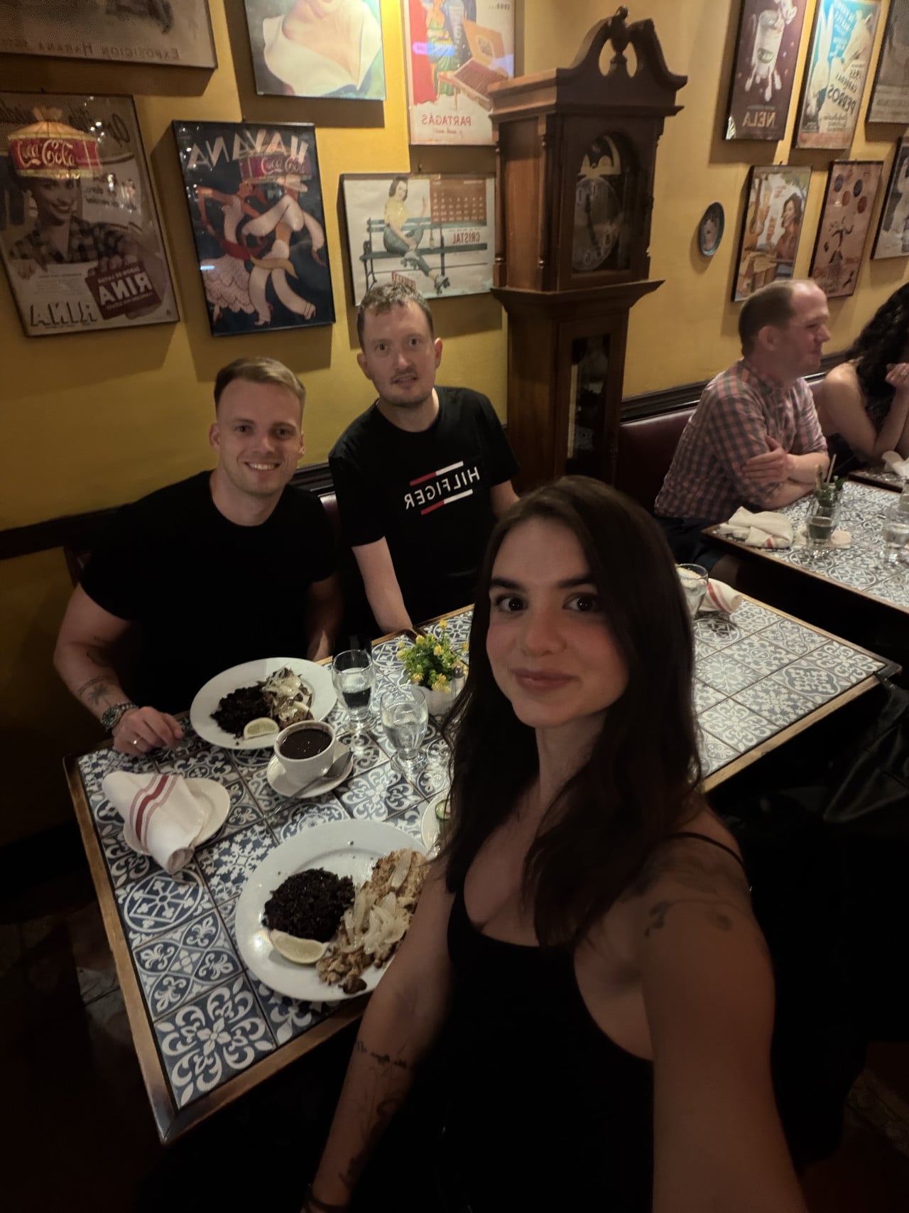 Skupina lidí pózuje u stolu v restauraci s retro plakáty na zdi.
