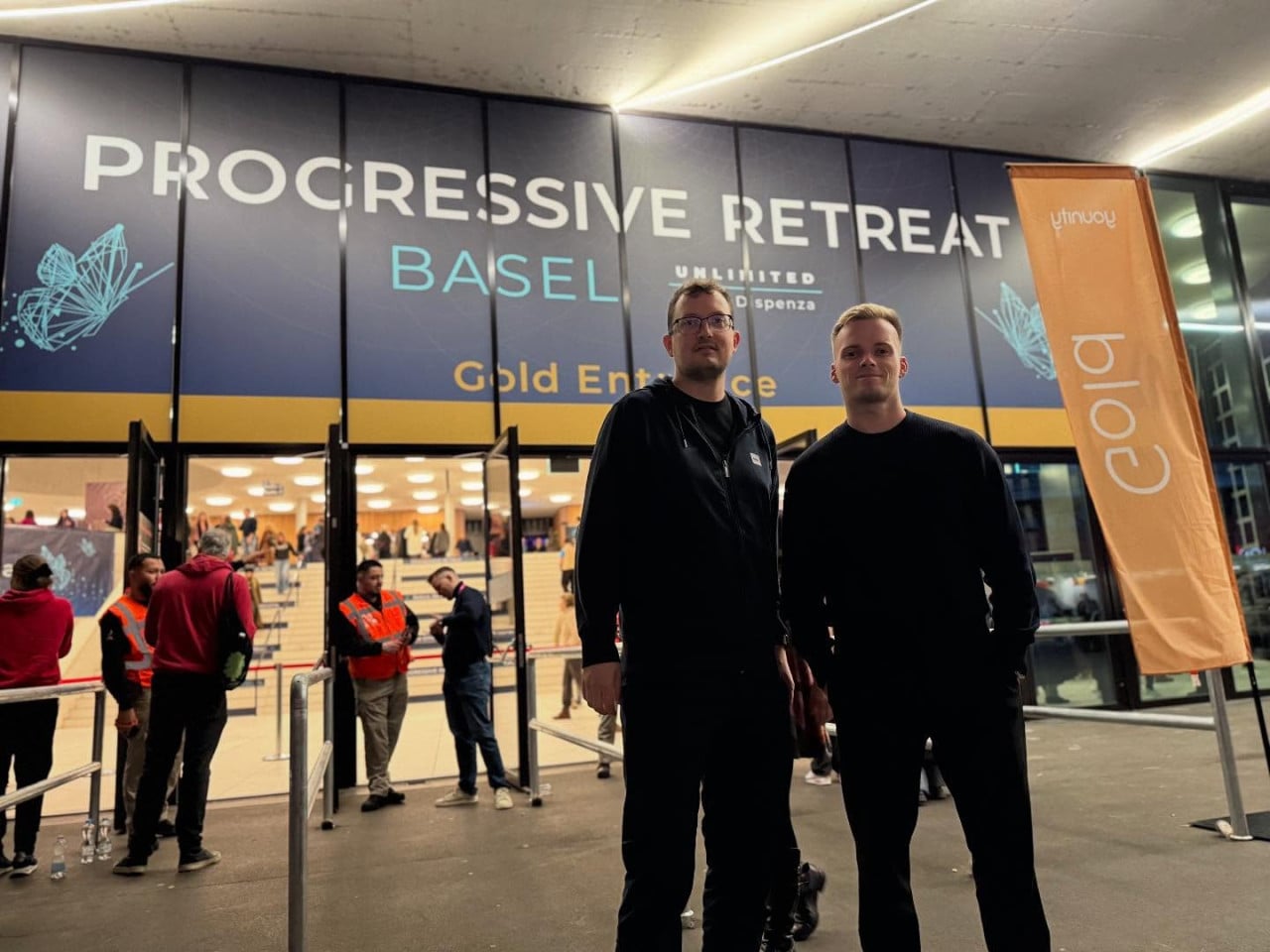 Dva muži stojí před budovou Progressive Retreat Basel u vstupu Gold Entrance.