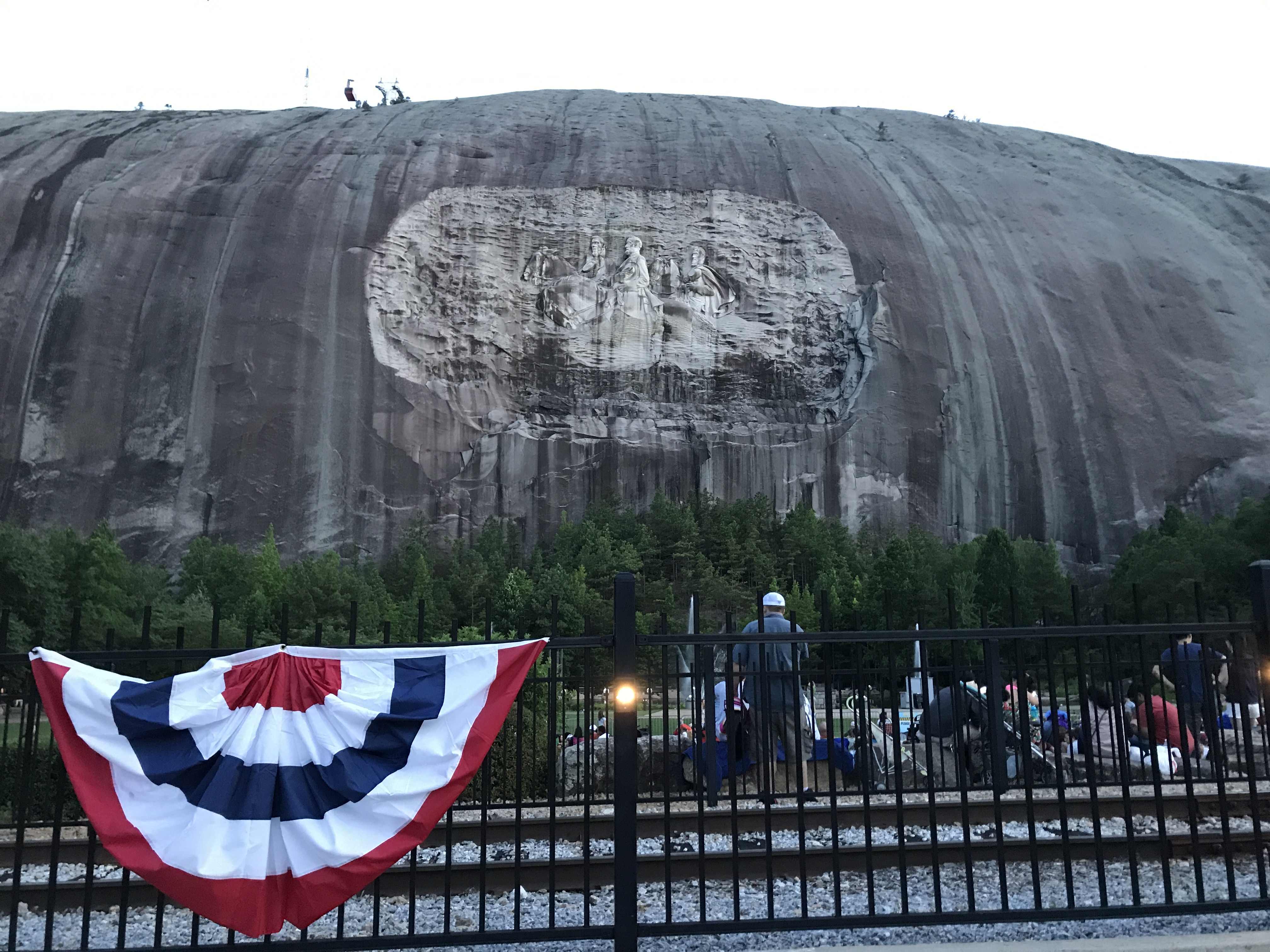 Reliéf tří jezdců vytesaný do Stone Mountain, v popředí plot s girlandou.