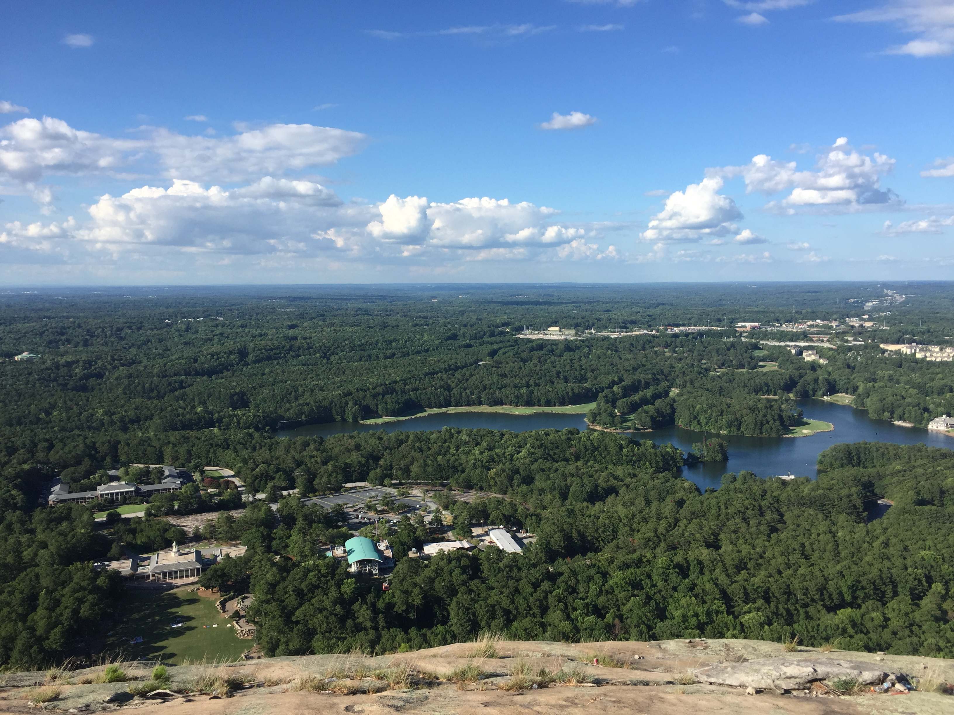 Výhled ze Stone Mountain na lesy, jezera a budovy pod modrou oblohou.