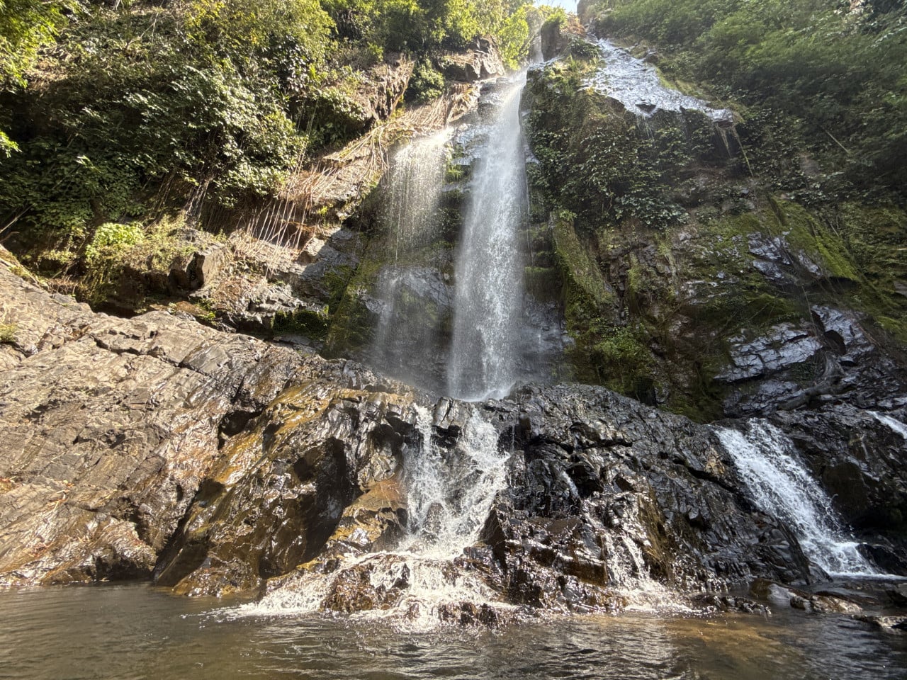 Vodopád stékající po tmavých skalách do jezírka, obklopený hustou džunglí.