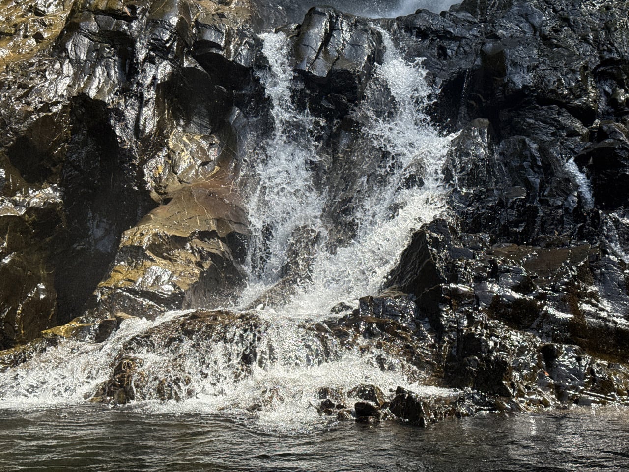 Voda stékající po tmavých skalách malého vodopádu do přírodního jezírka
