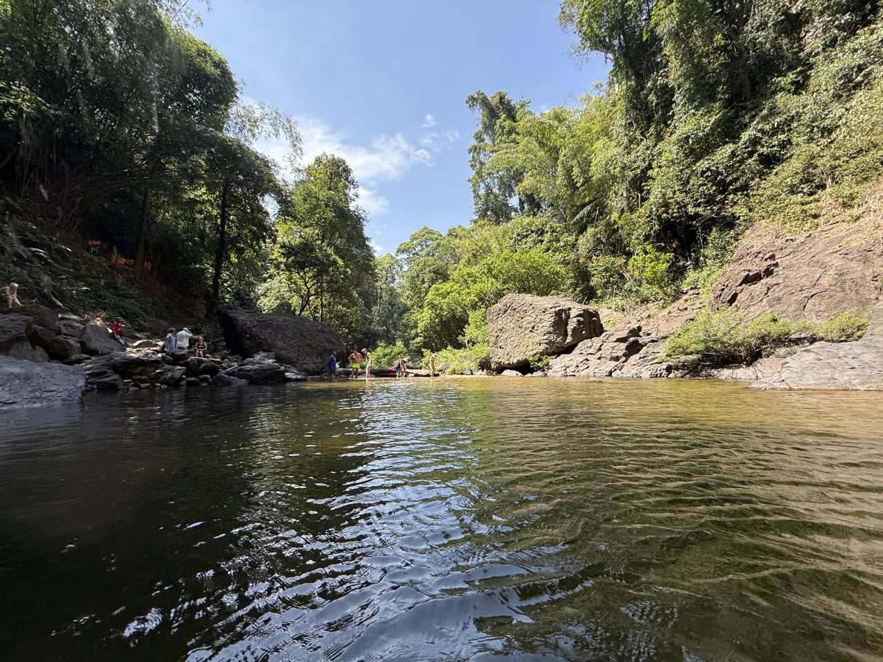 Přírodní jezírko pod vodopádem, lidé se koupou mezi balvany v džungli.