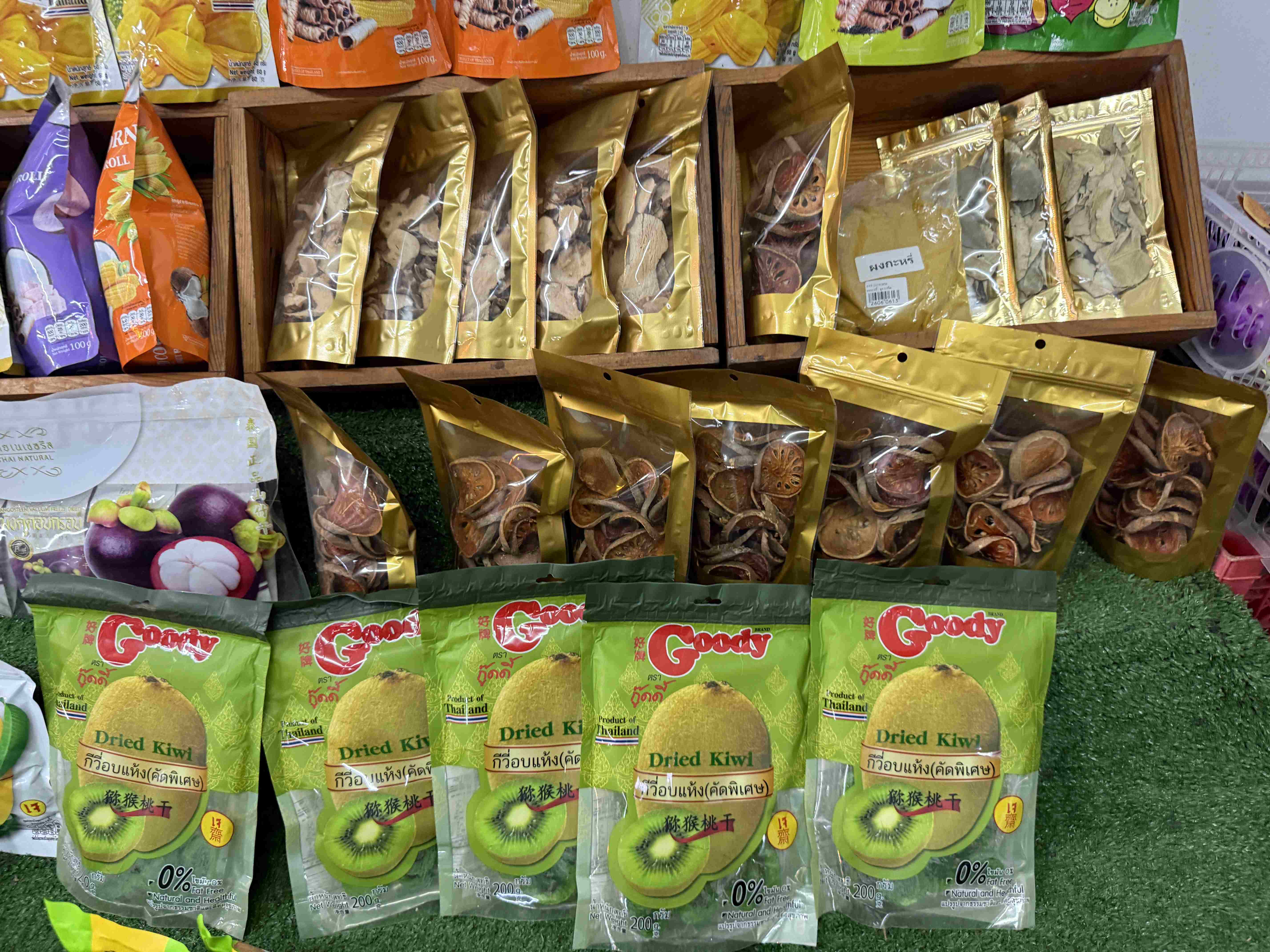 Regál s baleným sušeným ovocem; sáčky Goody Dried Kiwi a zlaté balíčky.