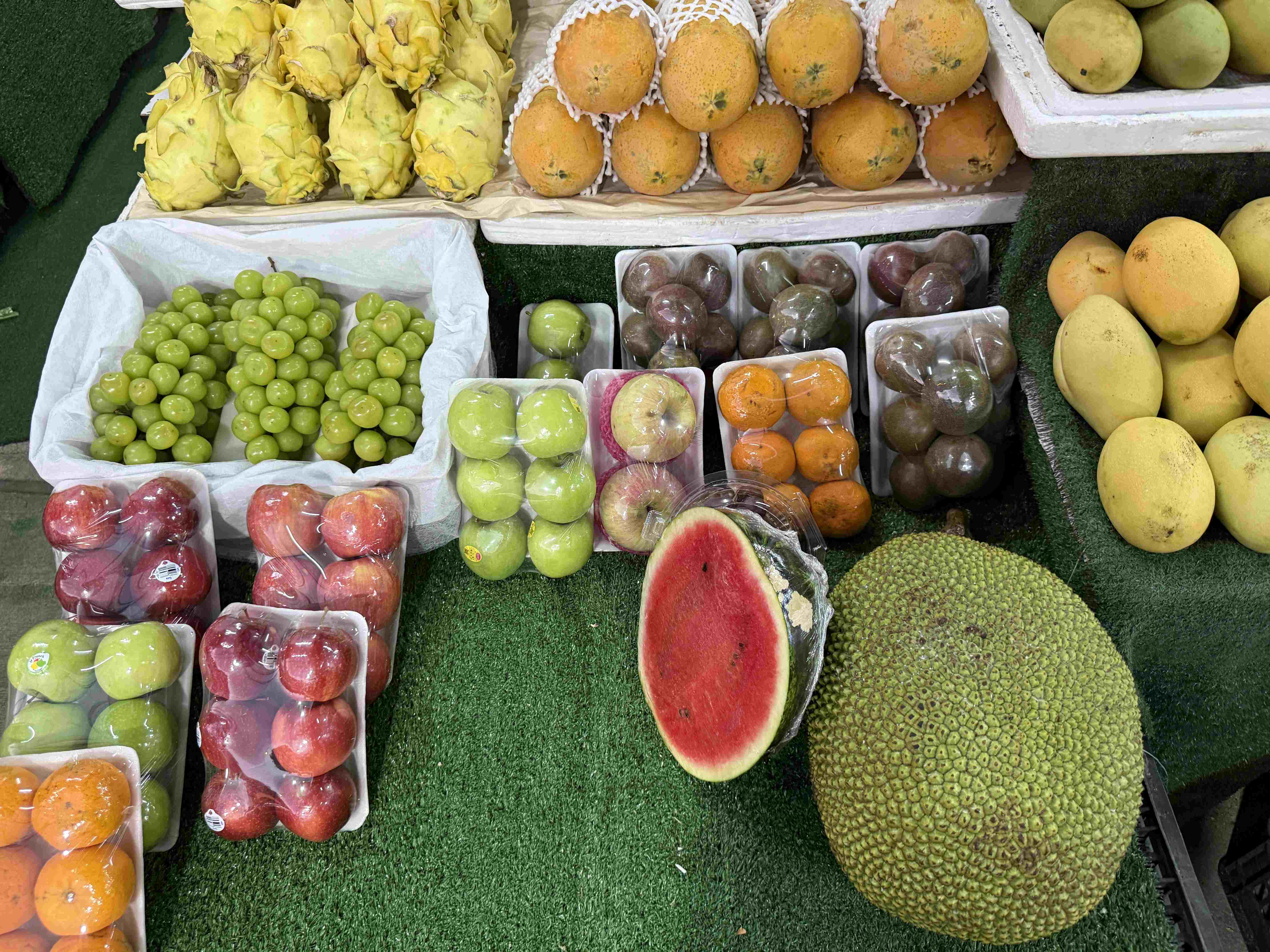 Stánek s tropickým ovocem: dračí plody, hrozny, jablka, mango, jackfruit, meloun.