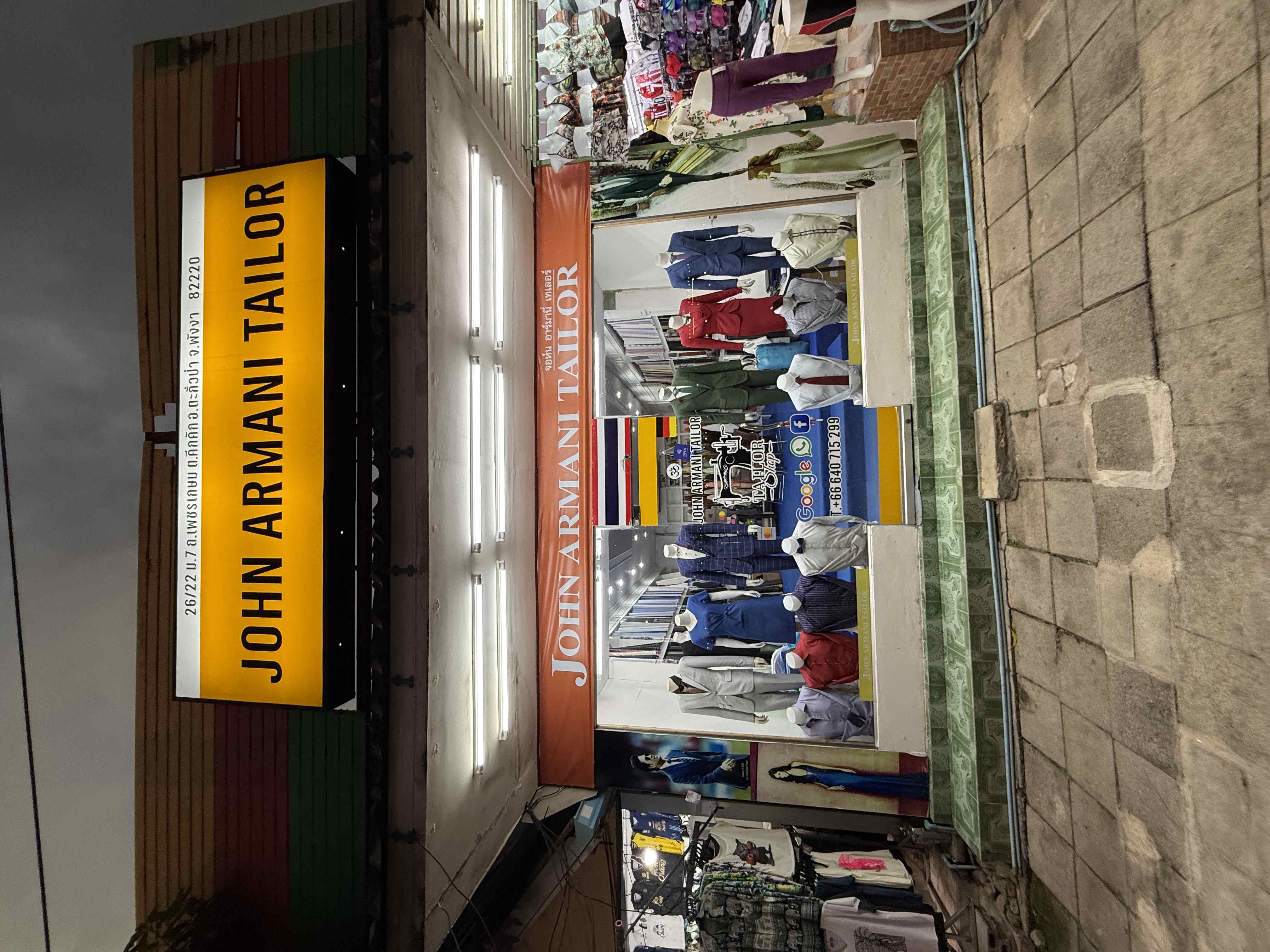 Obchod s nápisem JOHN ARMANI TAILOR, výloha s figurínami v oblecích.