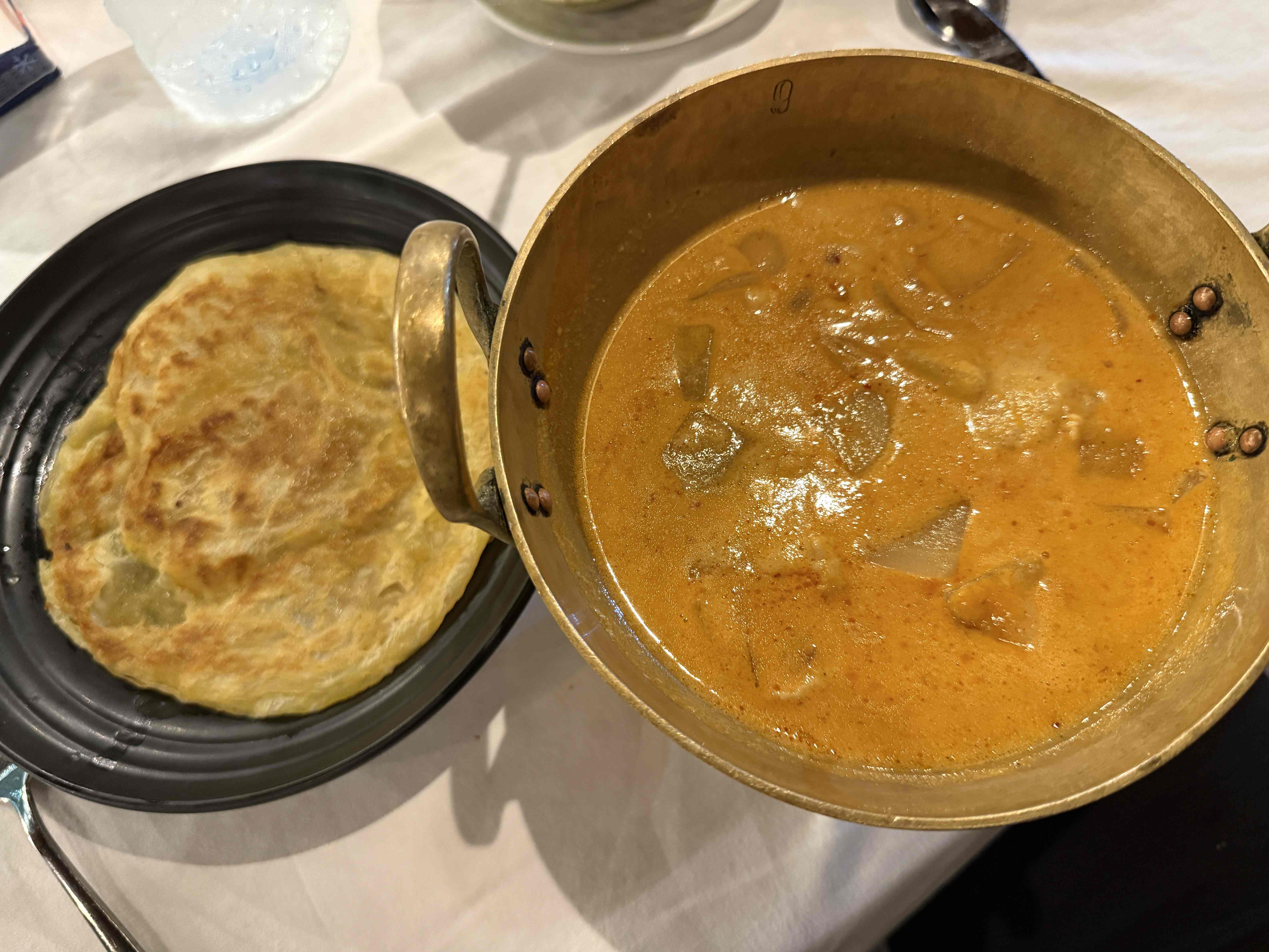 Miska thajského kari v mosazném hrnci a placka na černém talíři