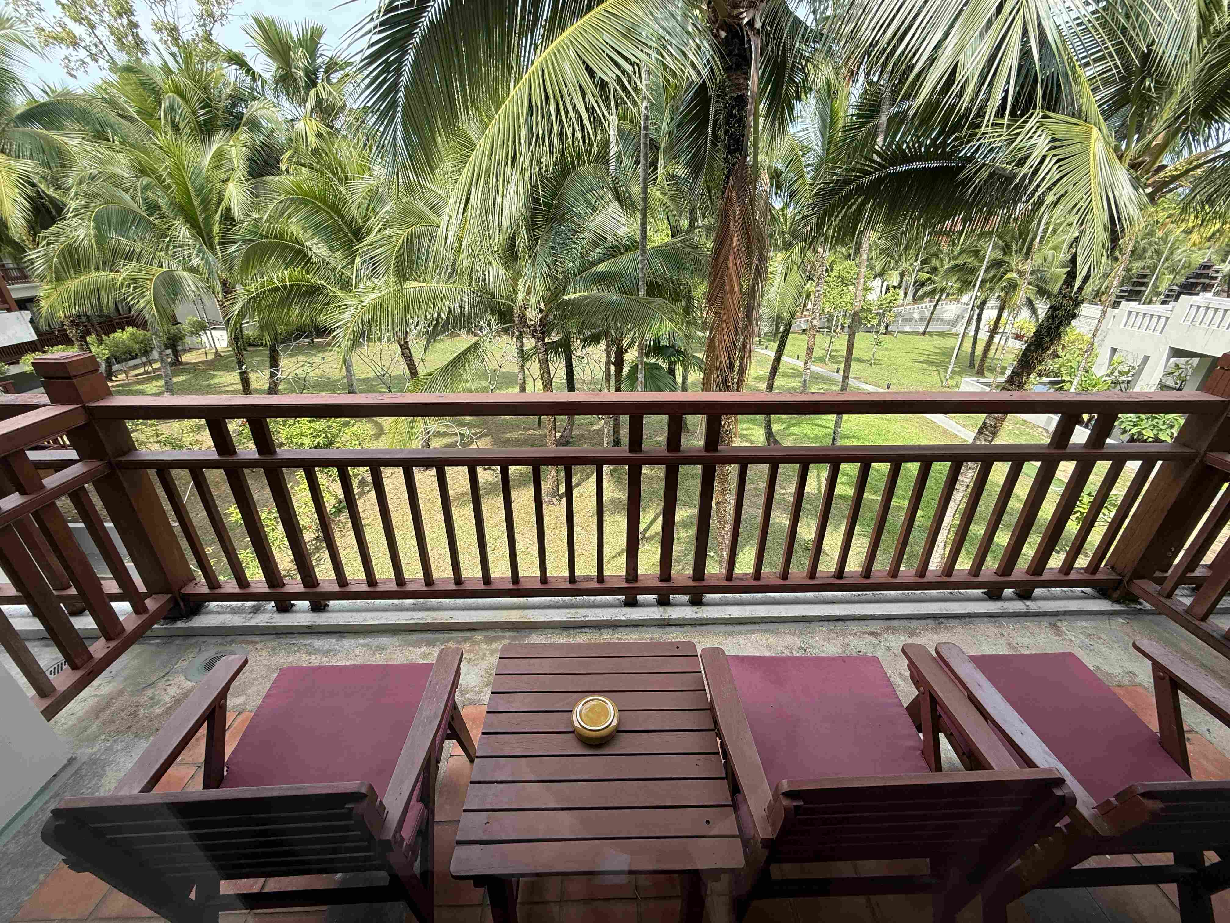 Balkon se dvěma lehátky, stolkem a výhledem na palmy a hotelovou zahradu.