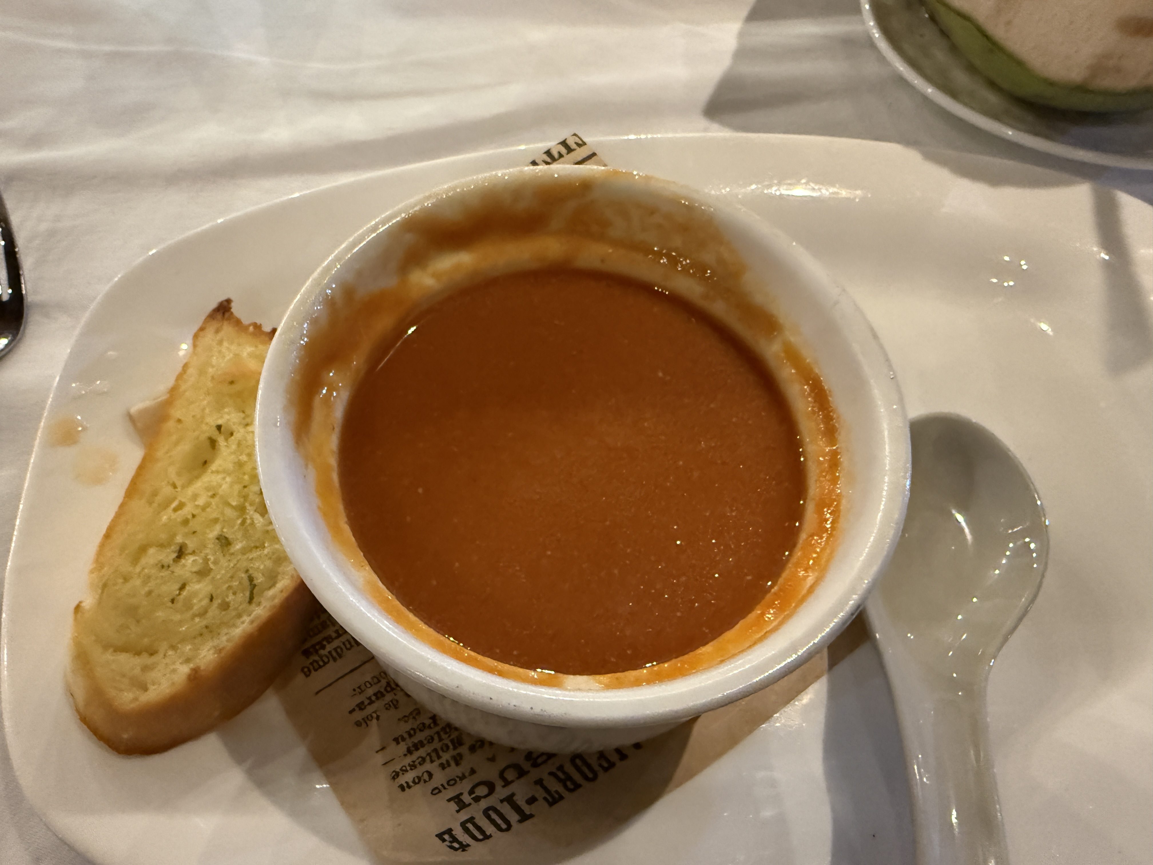 Miska rajčatové polévky na talíři s chlebem, lžící a ubrouskem s nápisem