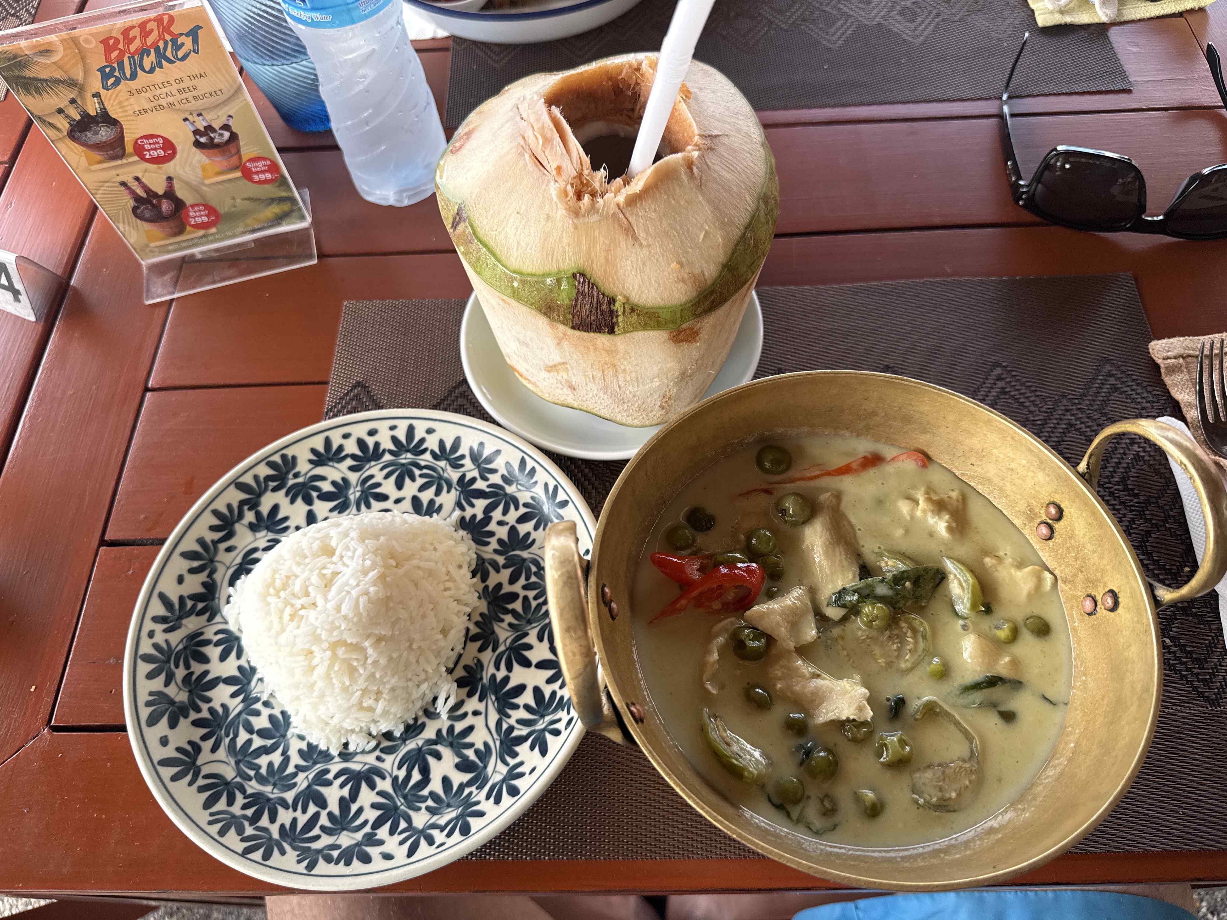 Talíř rýže, zelené kari v misce, kokos s brčkem, cedule BEER BUCKET.