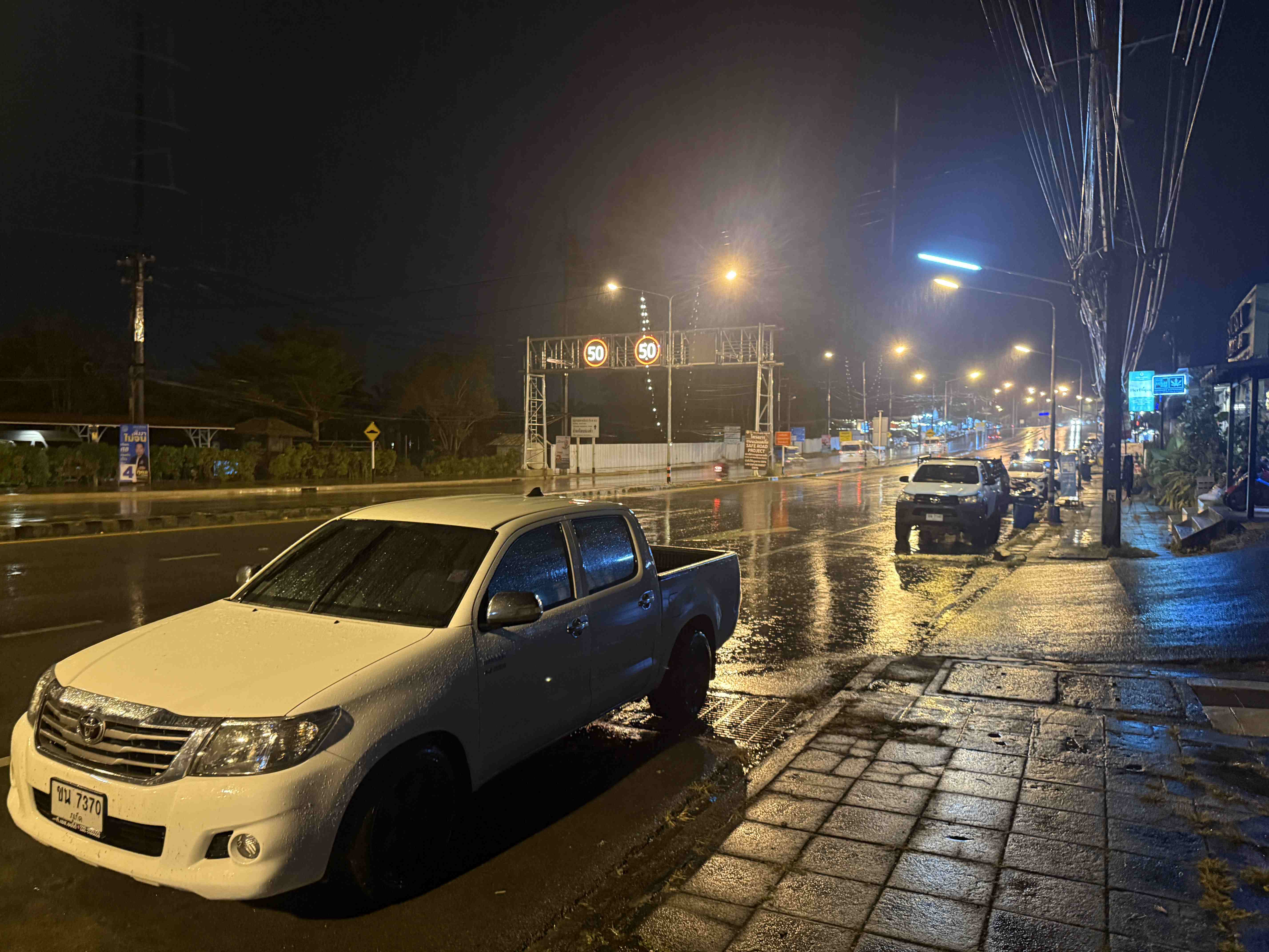 Deštivá noční ulice s mokrou vozovkou, zaparkovaným pickupem a značkou 50.