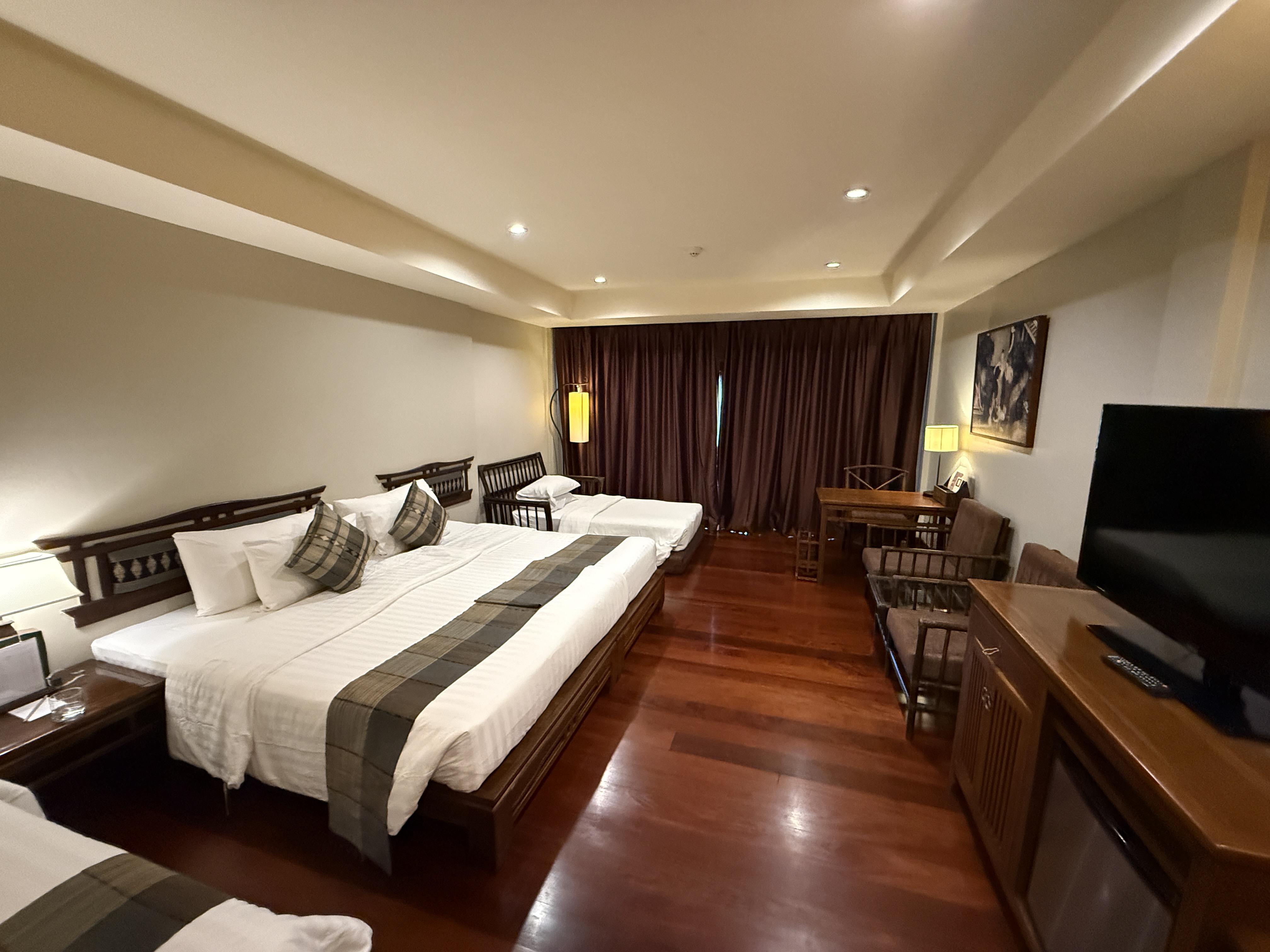 Hotelový pokoj s manželskou postelí a jednolůžkem, dřevěná podlaha, TV a závěsy