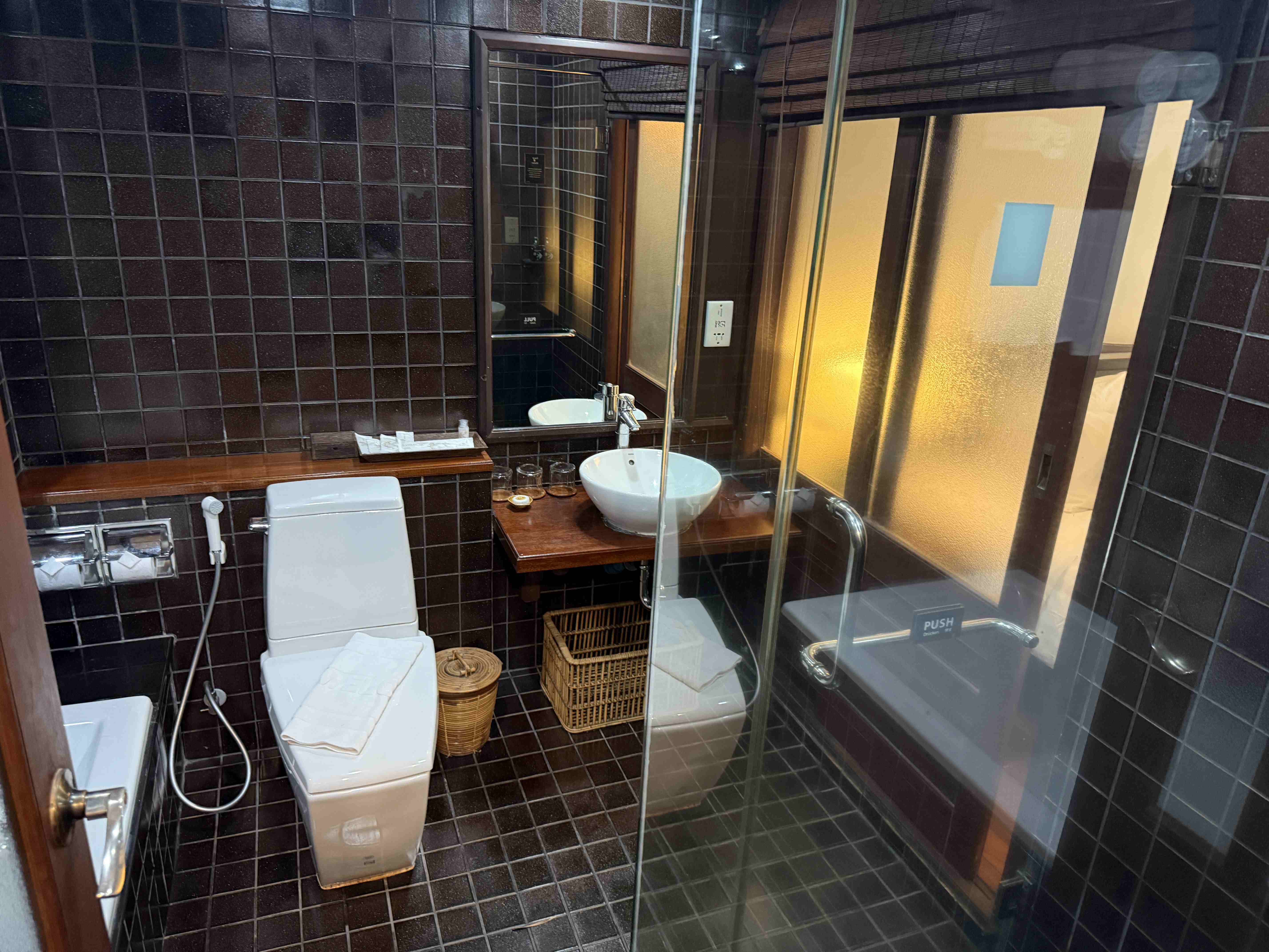 Koupelna s tmavými kachličkami, WC, umyvadlem, zrcadlem a vanou, nápis PUSH.