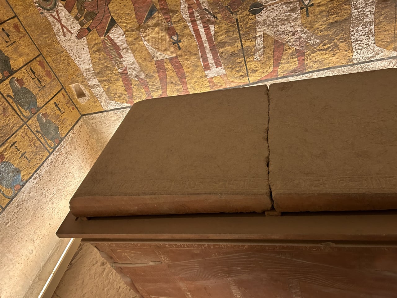 Detail kamenného sarkofágu v malované egyptské hrobce s hieroglyfy a postavami na stěnách