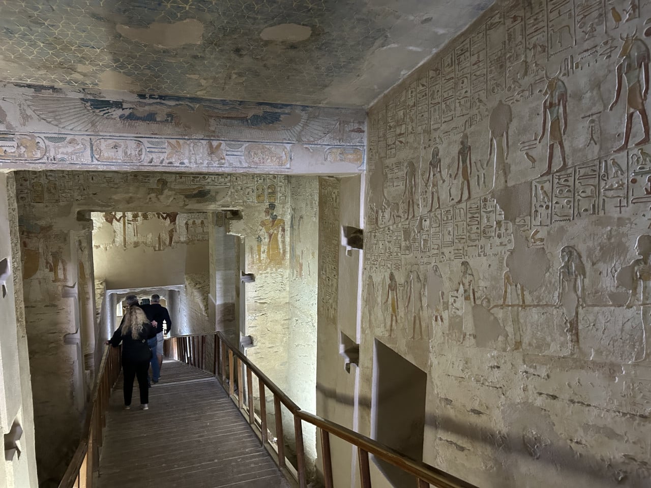 Chodba egyptské hrobky s barevnými hieroglyfy a návštěvníky na lávce