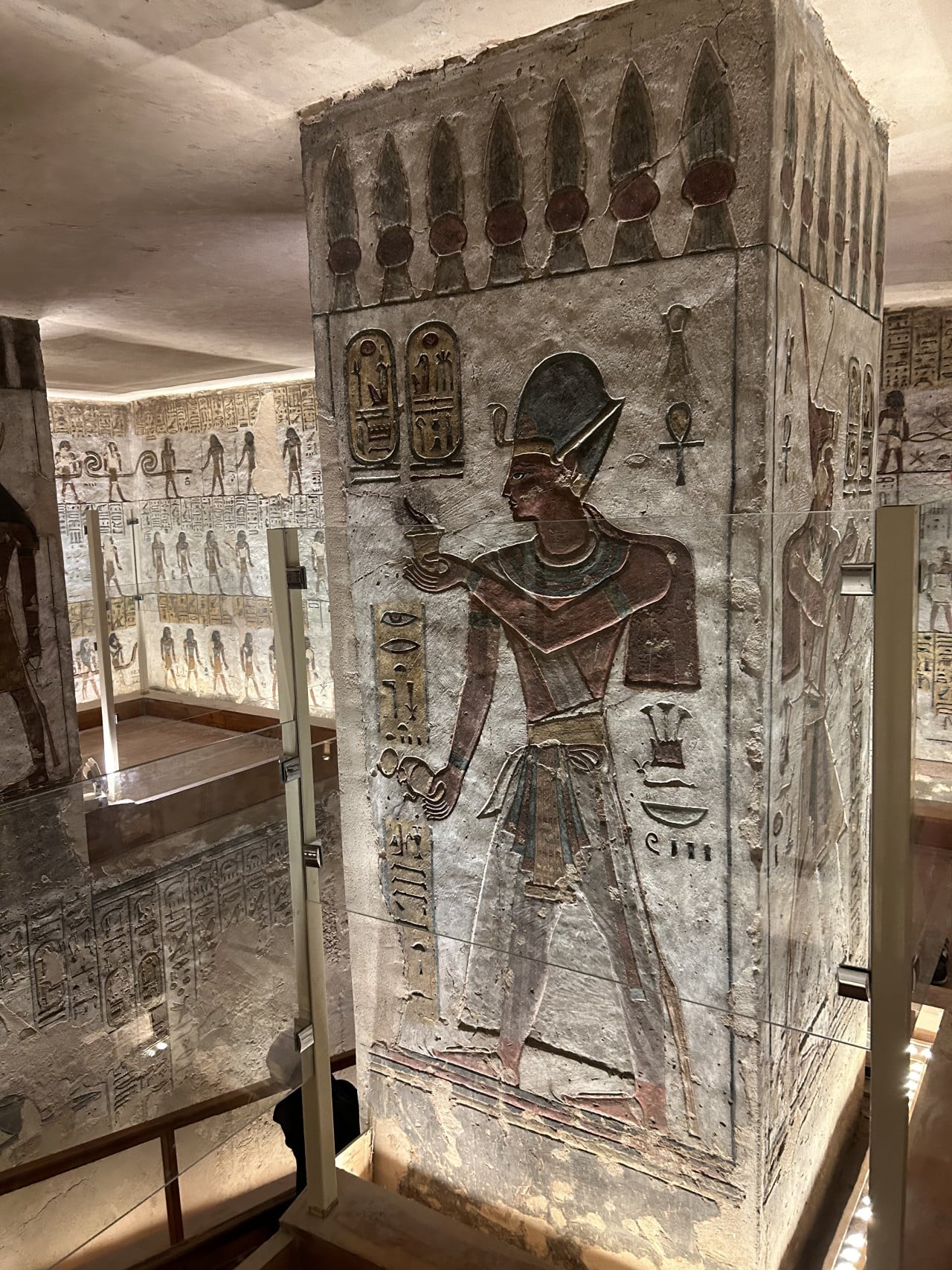 Malovaná egyptská hrobka s hieroglyfy a božstvem na kamenném pilíři