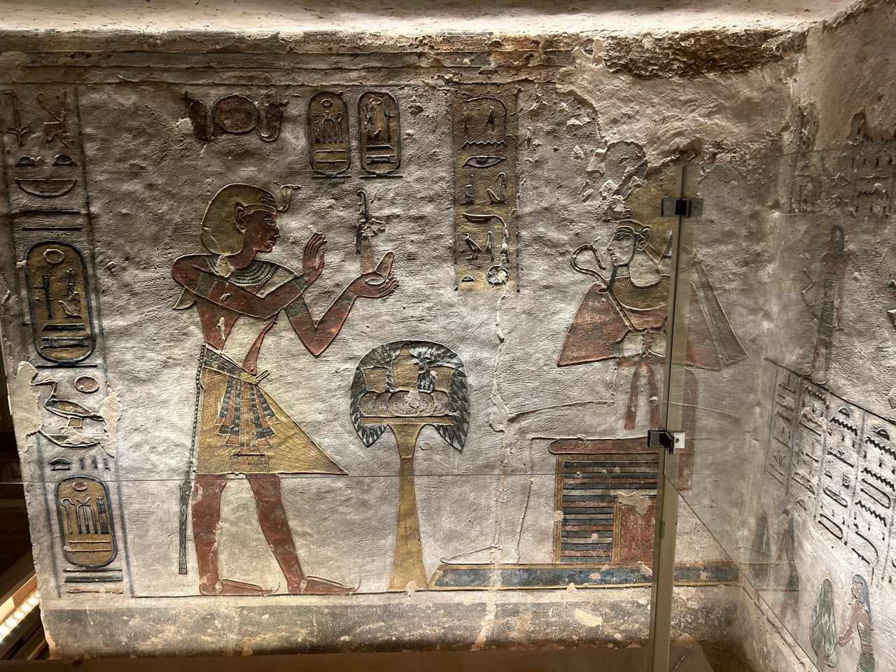 Barevná egyptská hrobková malba s hieroglyfy a postavami za sklem