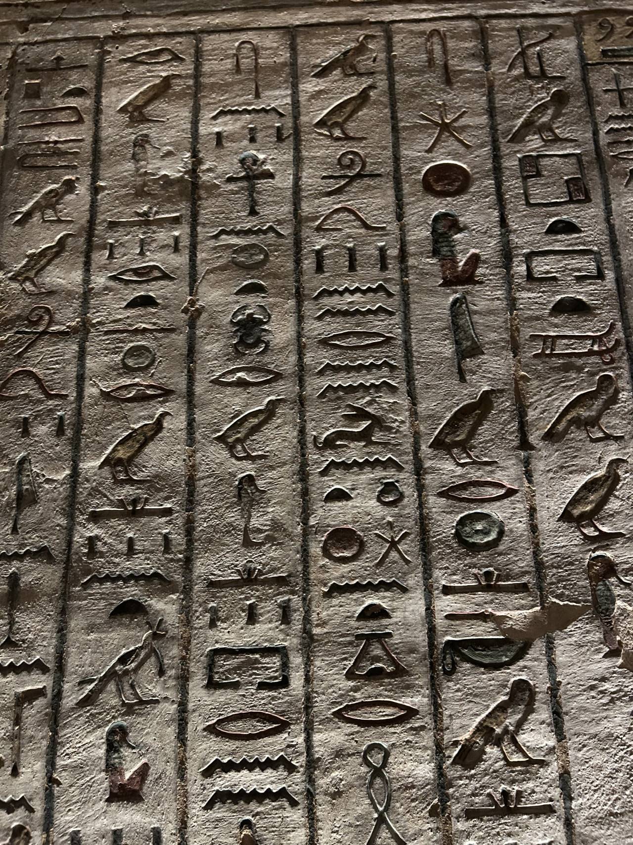 Vytesané egyptské hieroglyfy na kamenné stěně hrobky