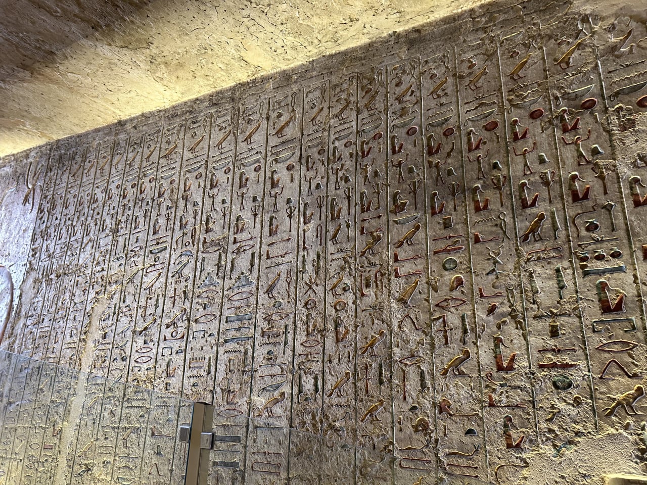 Barevná hieroglyfická stěna v egyptské hrobce s osvětleným stropem.
