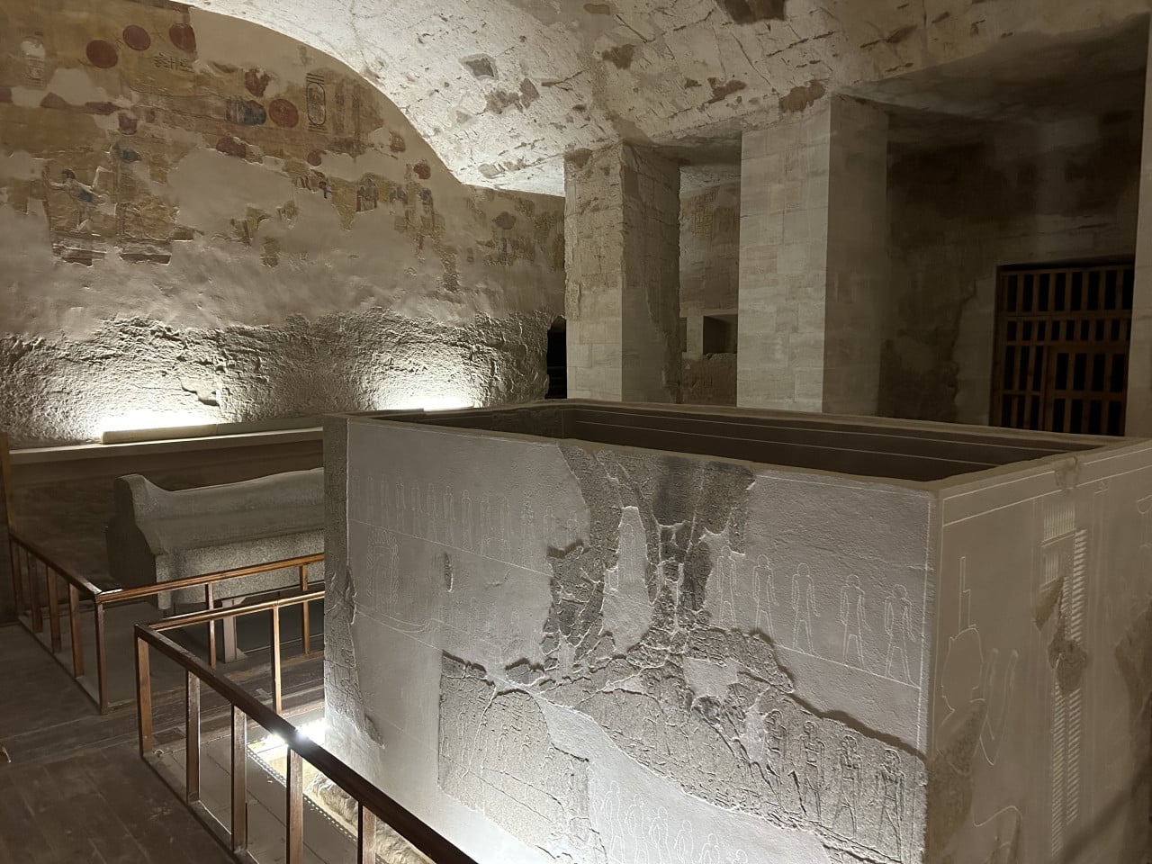 Kamenný sarkofág v hrobce s poničenými egyptskými reliéfy a osvětlenými zdmi