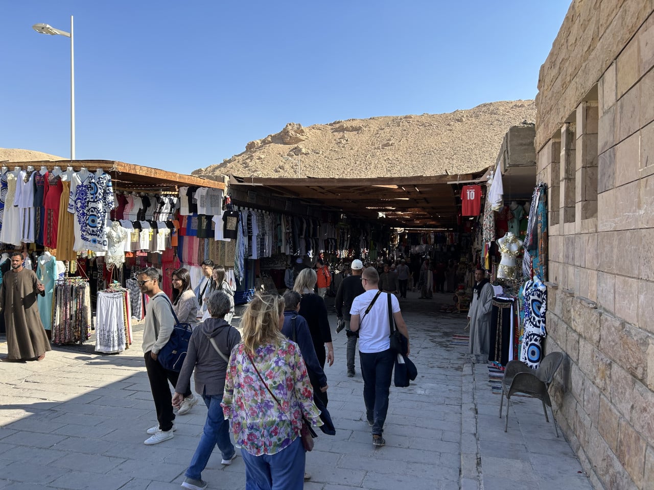 Turisté procházejí tržištěm s oblečením u skal v Údolí králů.