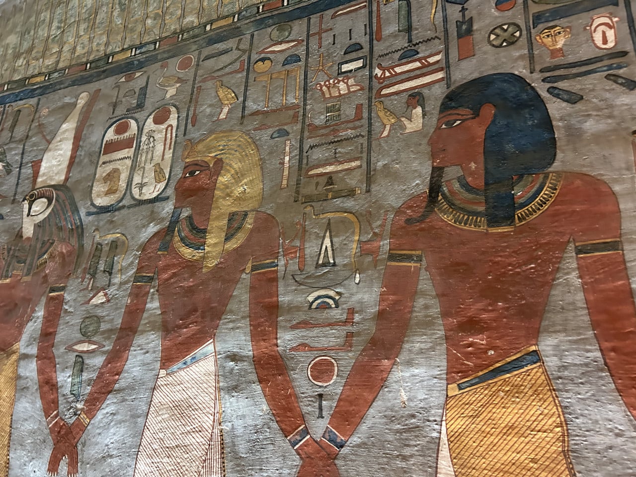 Barevná egyptská nástěnná malba se třemi postavami a hieroglyfy v hrobce.