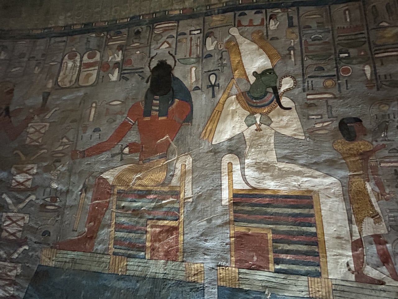 Barevná egyptská nástěnná malba s hieroglyfy a sedícími postavami božstev