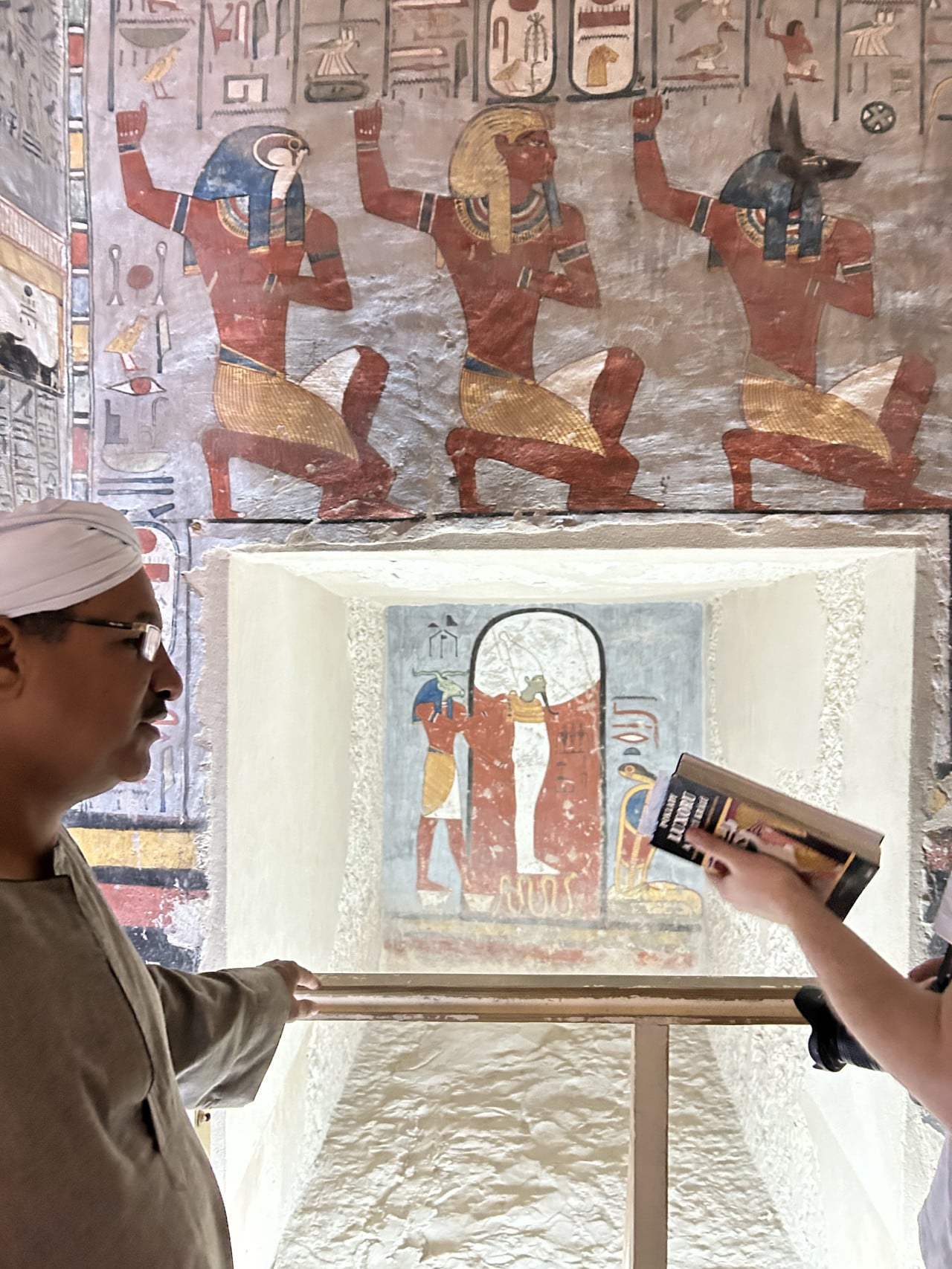 Nástěnné egyptské hieroglyfy a malby v hrobce, průvodce a návštěvníci u výmalby