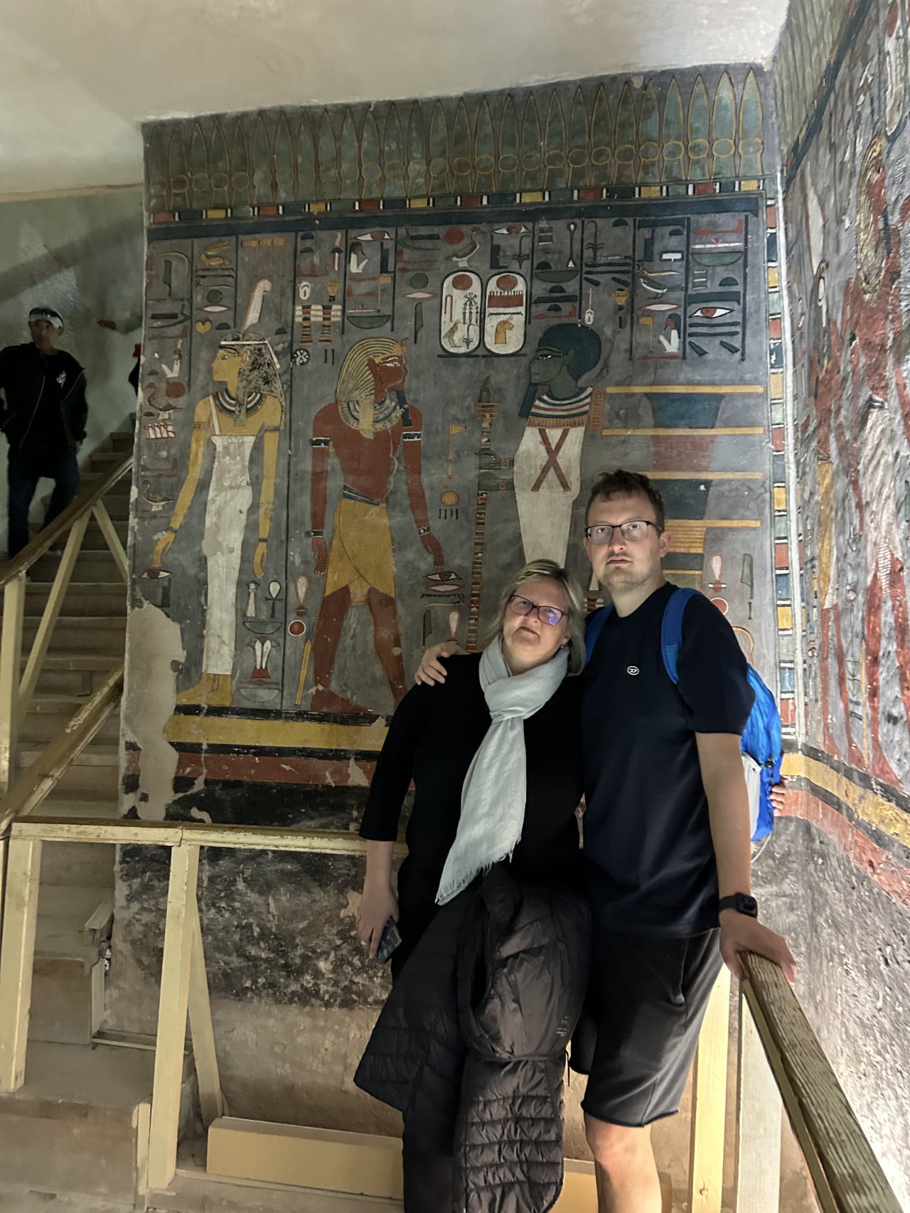 Turisté na schodišti před barevně zdobenou egyptskou hrobkou s hieroglyfy.