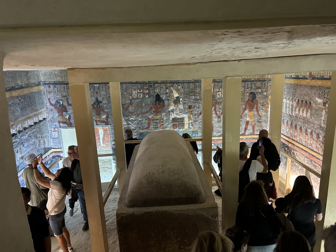 Turisté uvnitř hrobky v Údolí králů, barevné egyptské malby na stěnách a sarkofág uprostřed