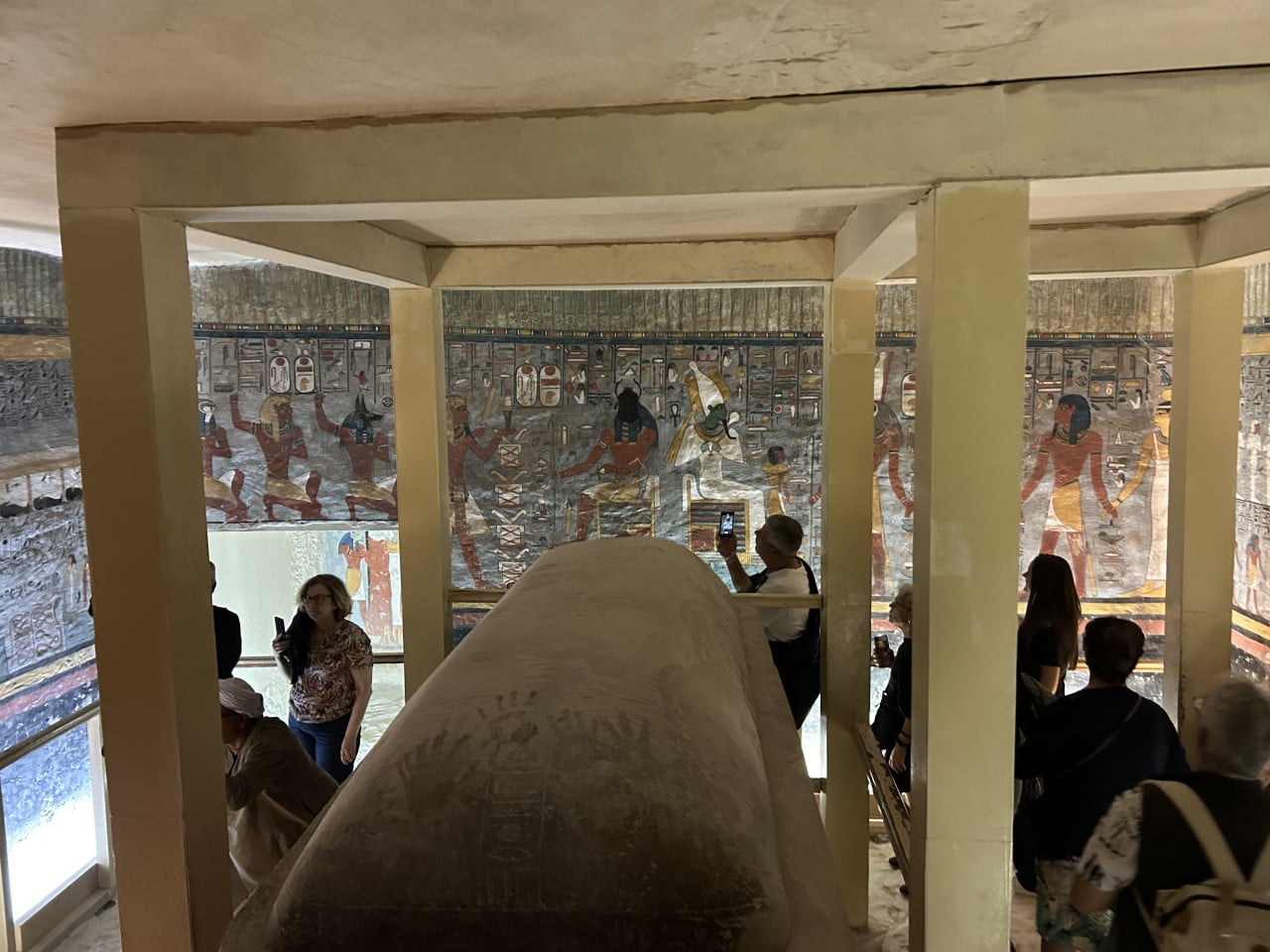 Návštěvníci v hrobce s barevnými egyptskými malbami a kamenným sarkofágem