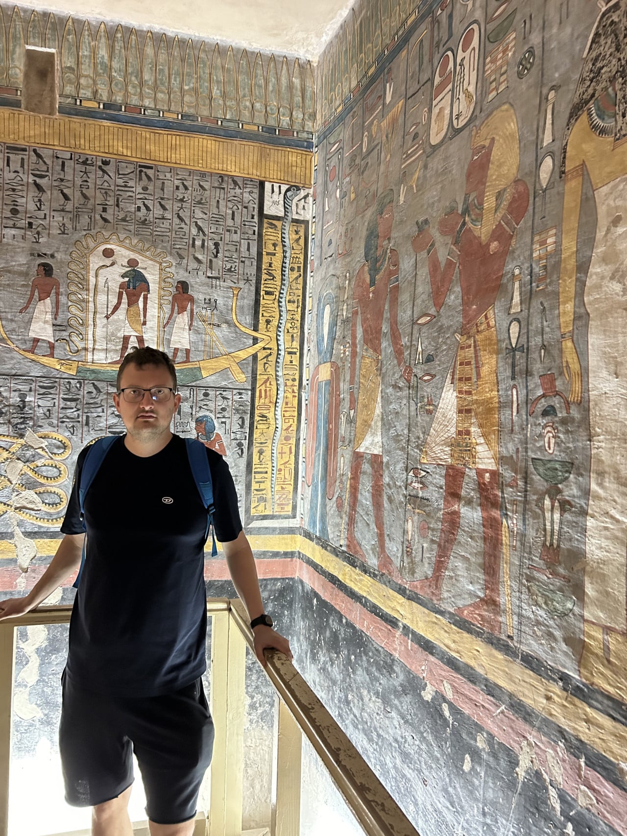 Muž stojí v egyptské hrobce u barevných hieroglyfických maleb.