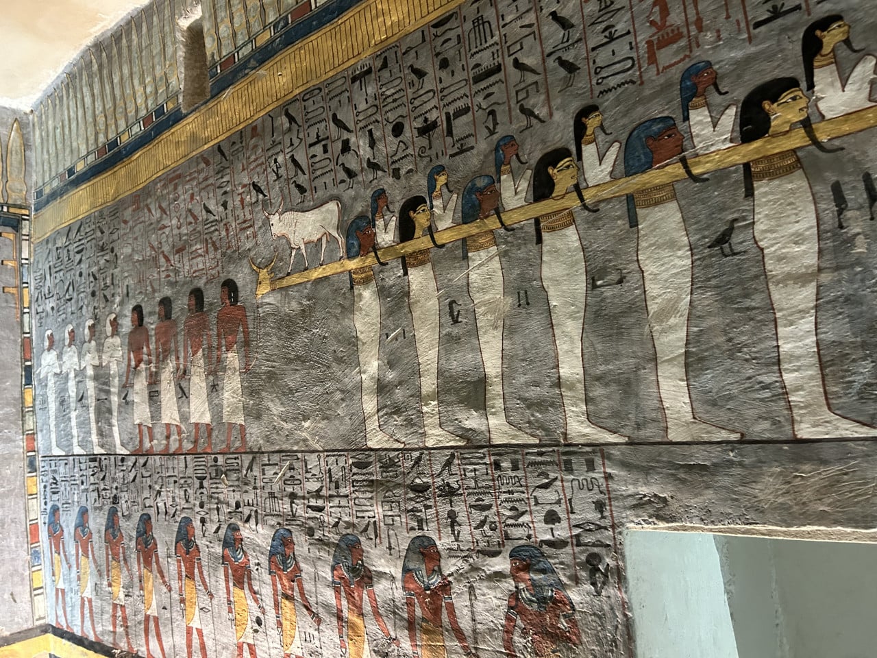 Barevná egyptská nástěnná malba s hieroglyfy a postavami v hrobce.