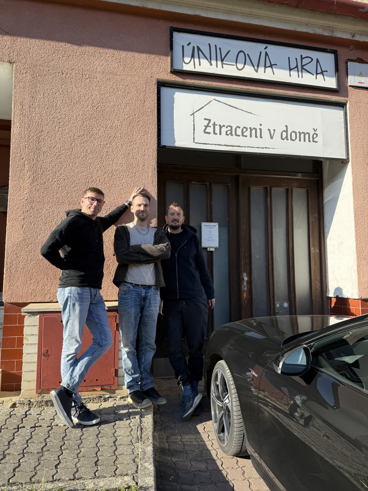 Tři muži před vchodem únikové hry Ztraceni v domě v Brně, nápis Úniková hra.