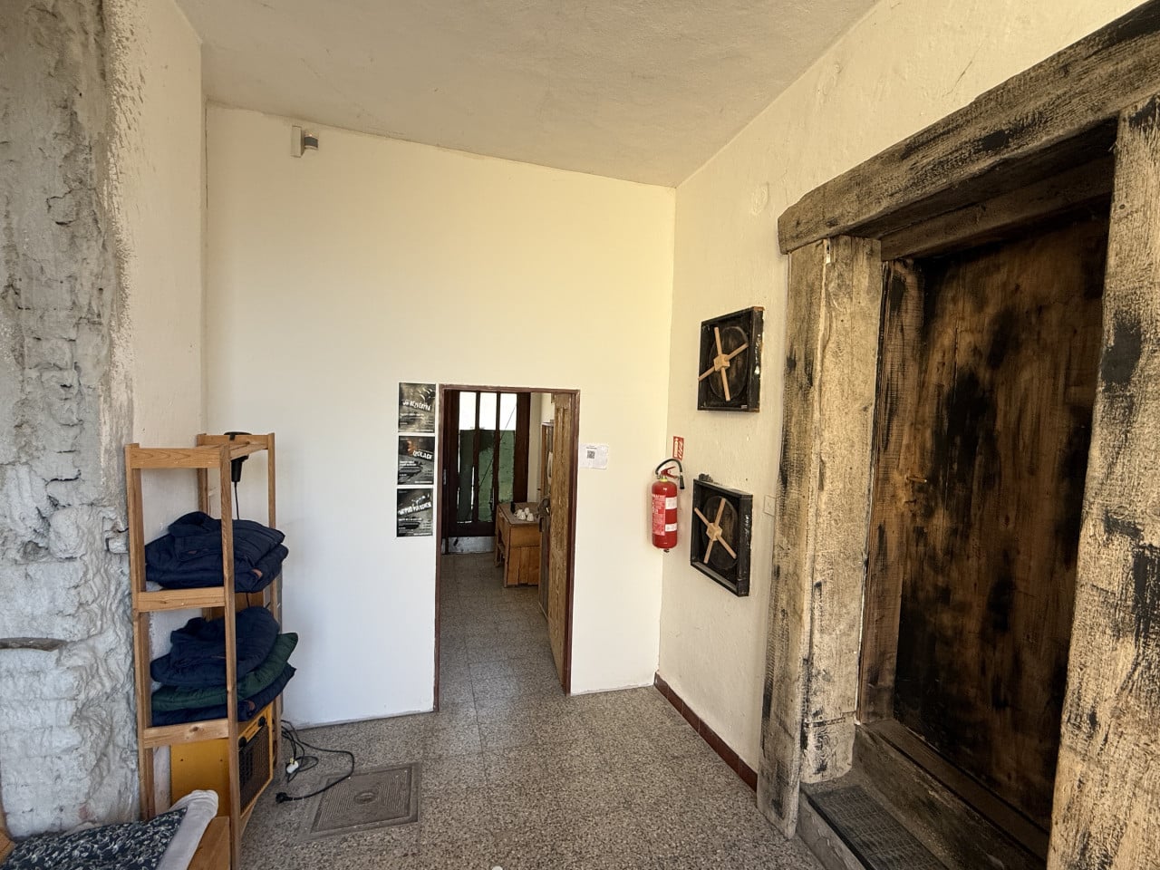 Interiér únikové hry s dřevěnými dveřmi, ventily, hasicím přístrojem a policí s oblečením.