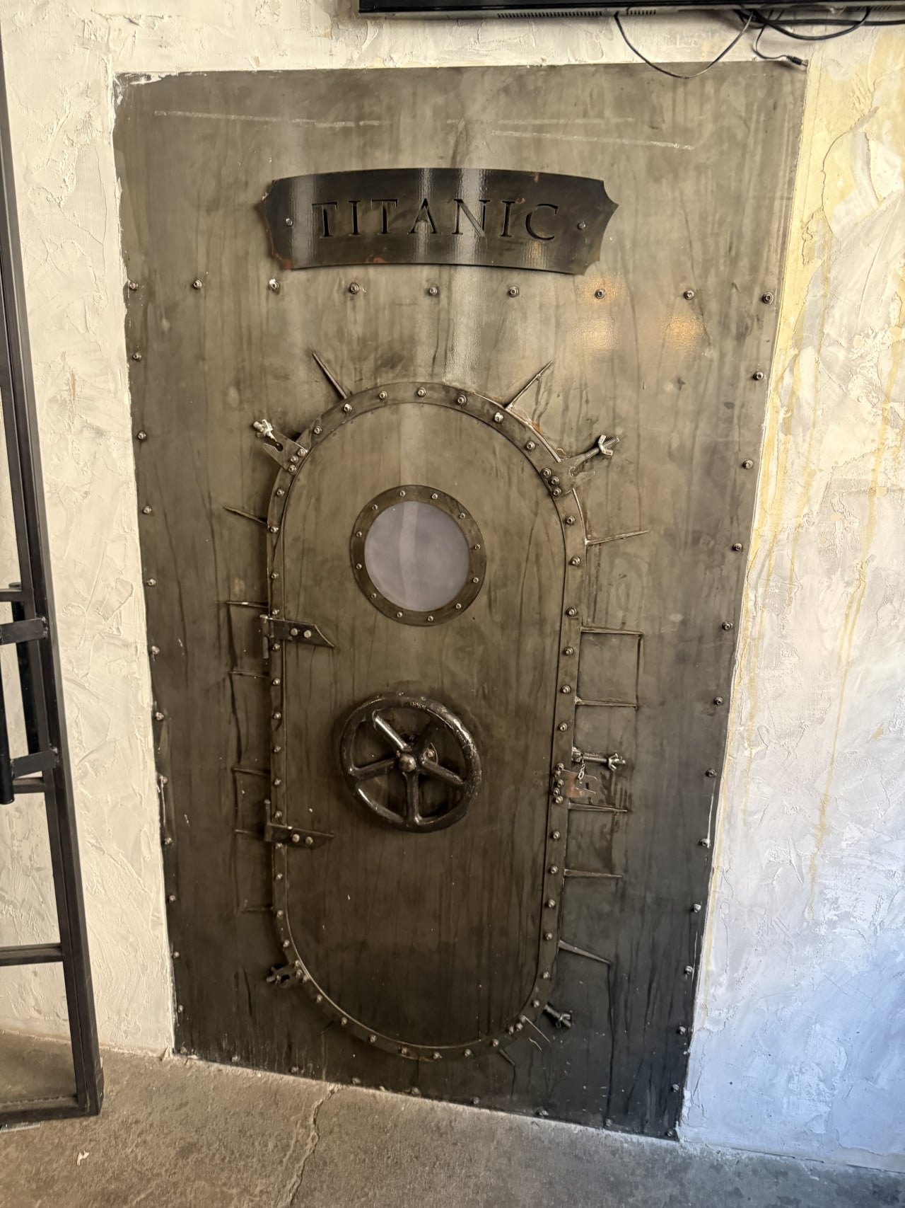 Temné kovové dveře trezoru s nápisem TITANIC a otočným kolem.