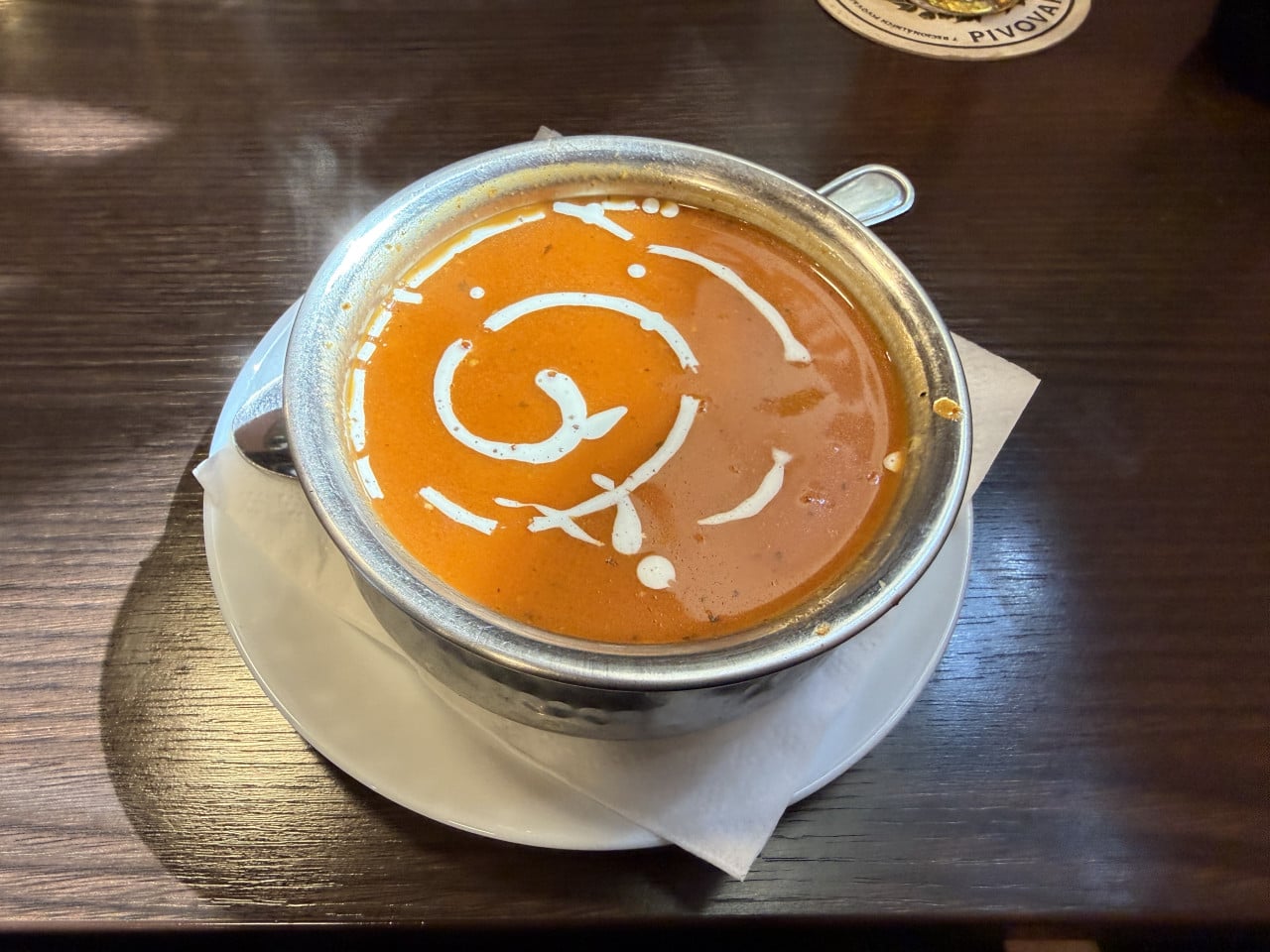 Miska rajčatové polévky se smetanovým spirálovým vzorem na bílém talíři.