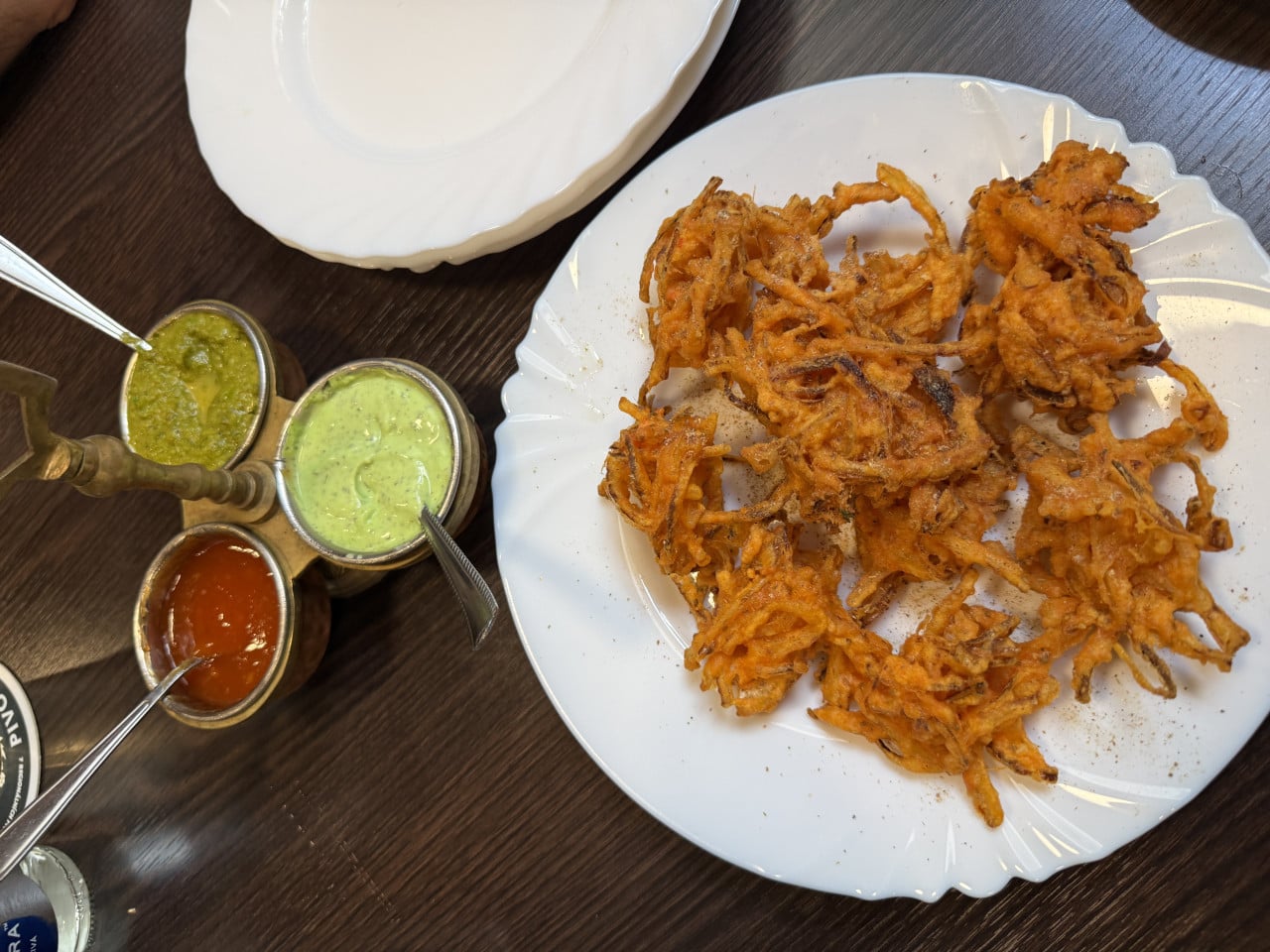 Talíř smažené cibule se třemi omáčkami na stole.