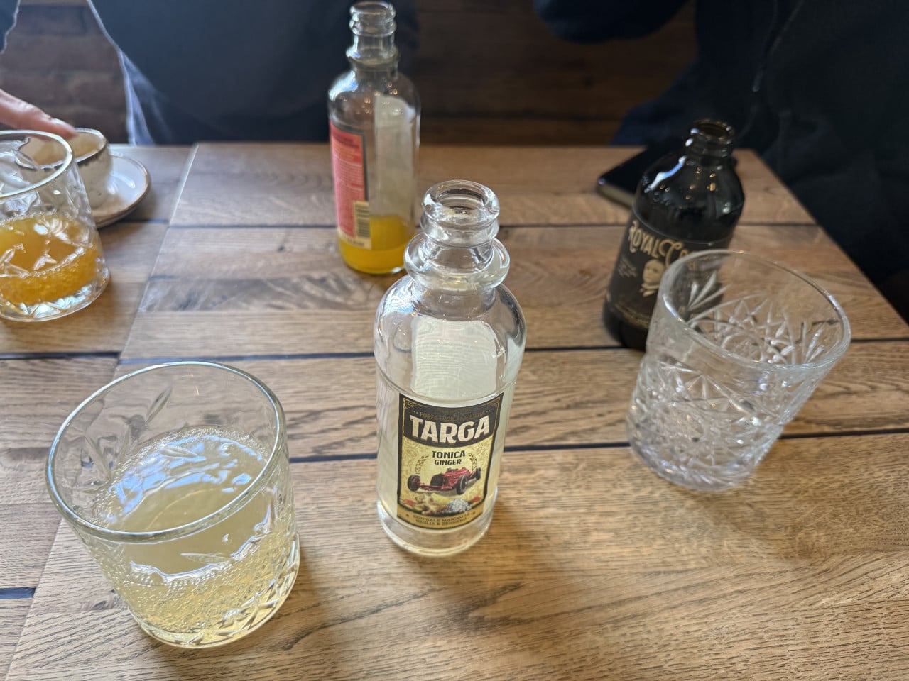 Láhev Targa Tónica Ginger mezi sklenkami s nápoji na dřevěném stole