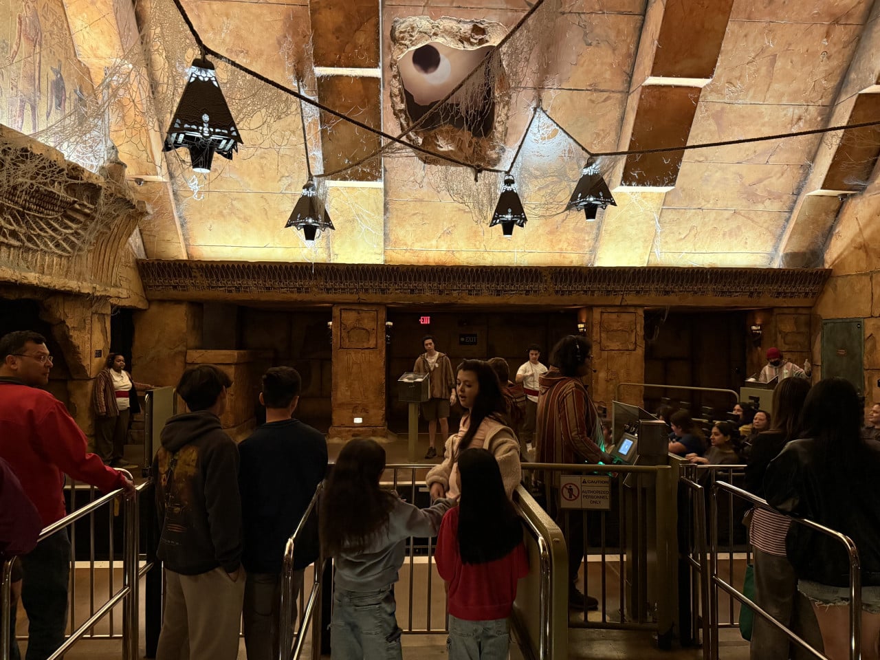 Návštěvníci čekají ve stanici s hnědými kamennými stěnami a visícími lampami.