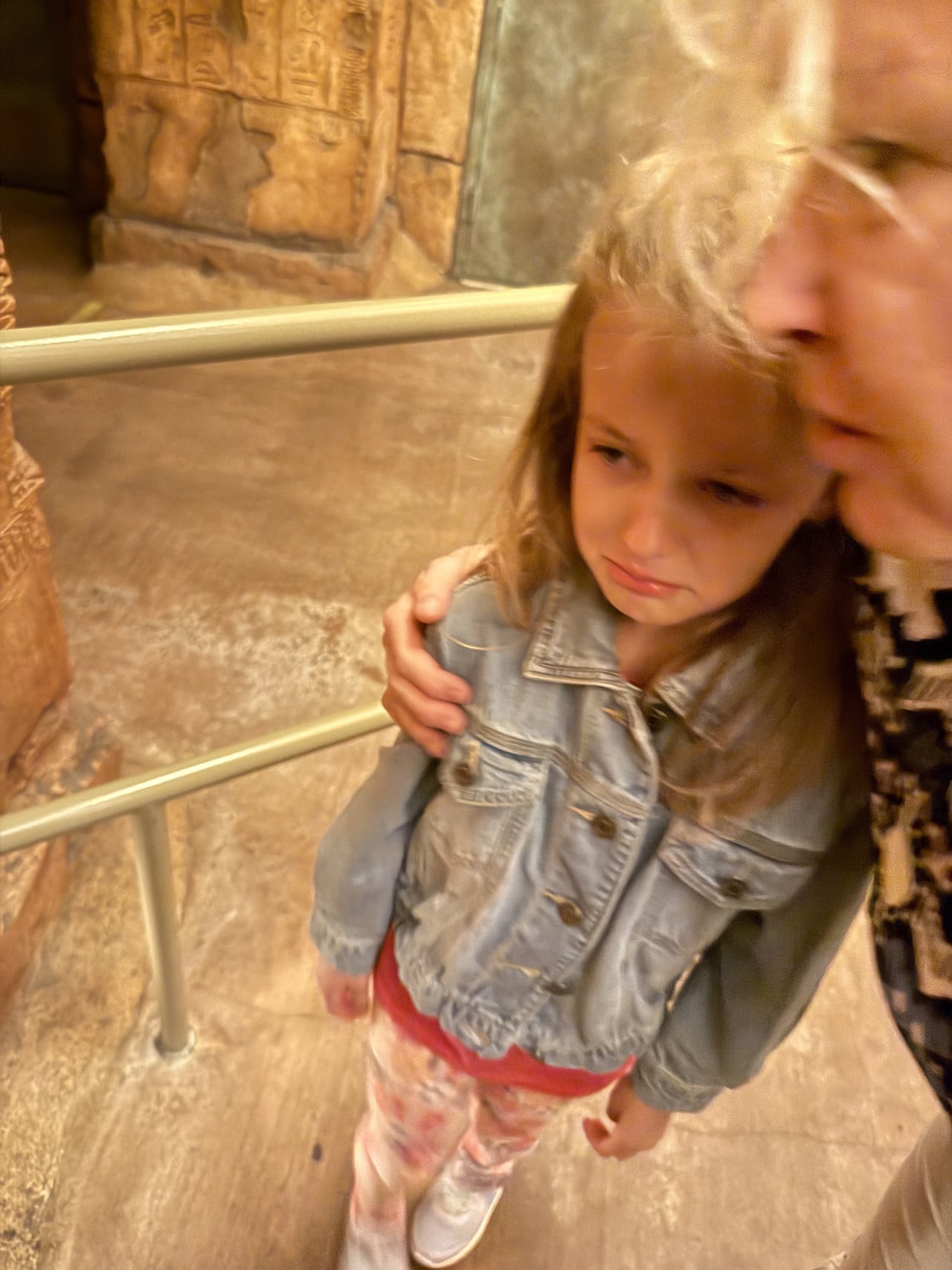 Plačící dívka v džínsové bundě v objetí dospělého v interiéru Universal Studios.