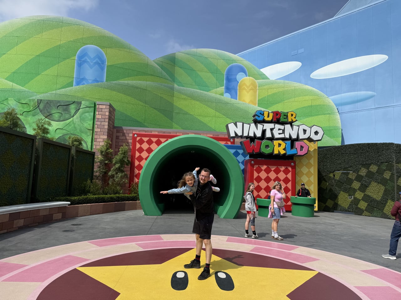 Vstup do Super Nintendo World v Universal Studios, muž nese dítě před barevným portálem.