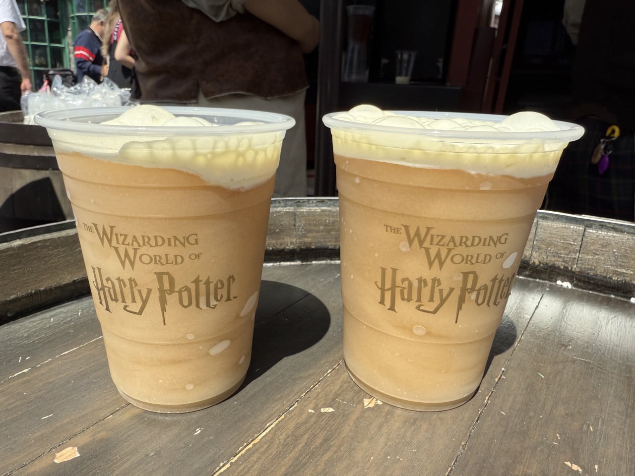 Dva kelímky máslového ležáku The Wizarding World of Harry Potter na dřevěném stole.