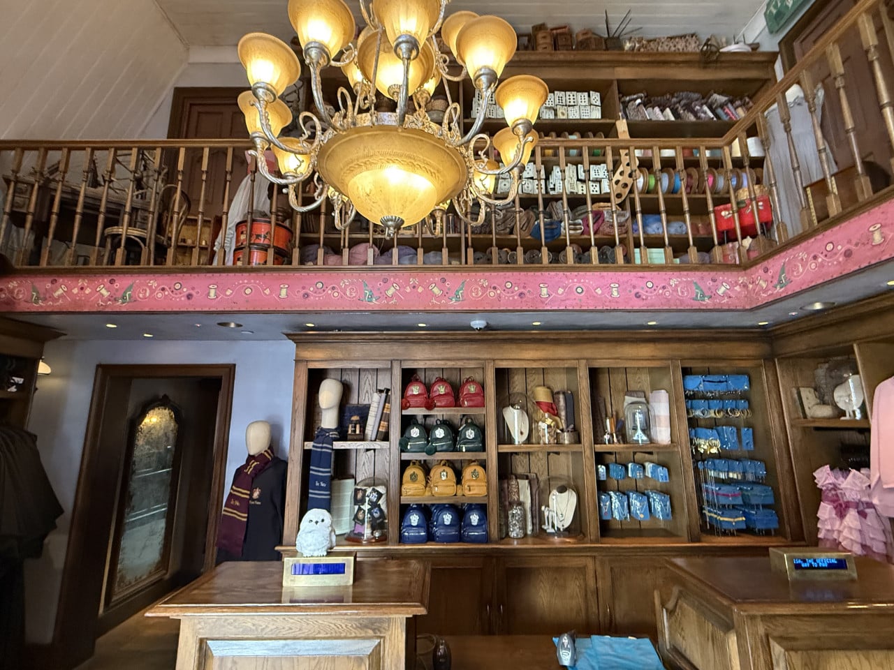 Obchod s Harry Potter suvenýry, dřevěné police, svítící lustr a modro-červené šály.