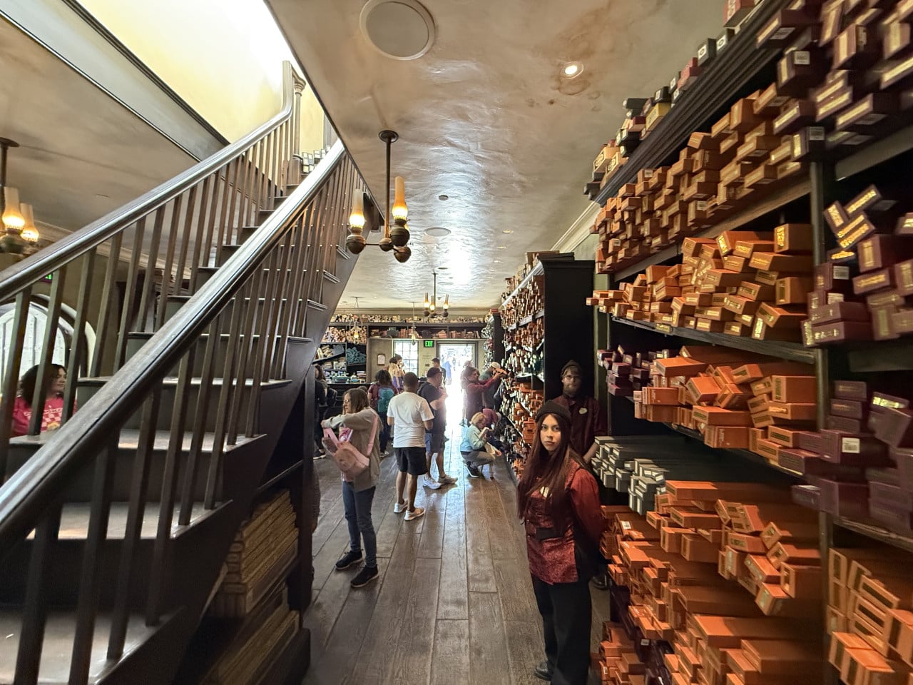 Interiér kouzelnického obchodu s policemi plnými krabiček a návštěvníky.