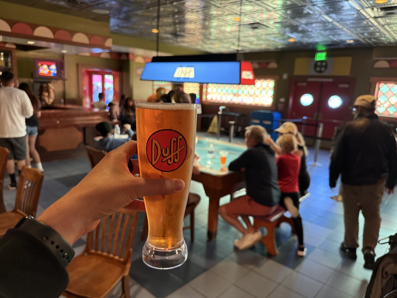 Ruka drží sklenici máslového ležáku Duff v tematickém baru Universal Studios.