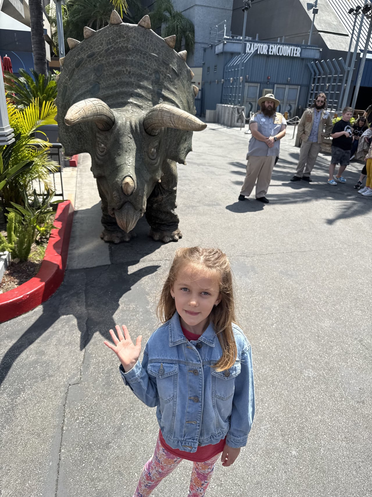 Dívka v džínové bundě mává u atrapy triceratopse v Universal Studios Hollywood