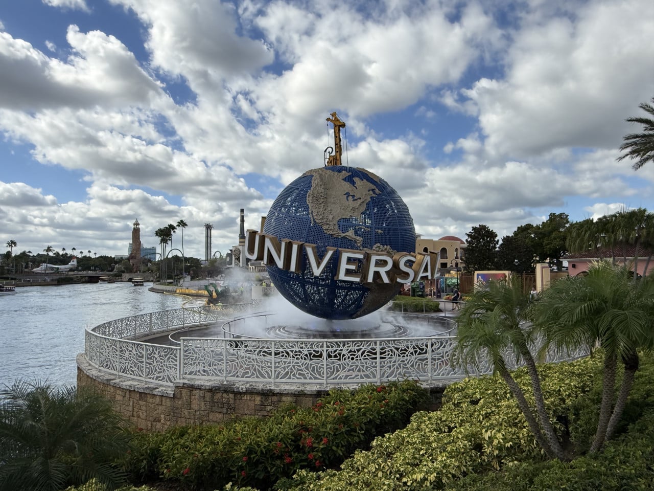 Vstupní glóbus Universal Studios Orlando s vodními tryskami a palmami pod oblačnou oblohou