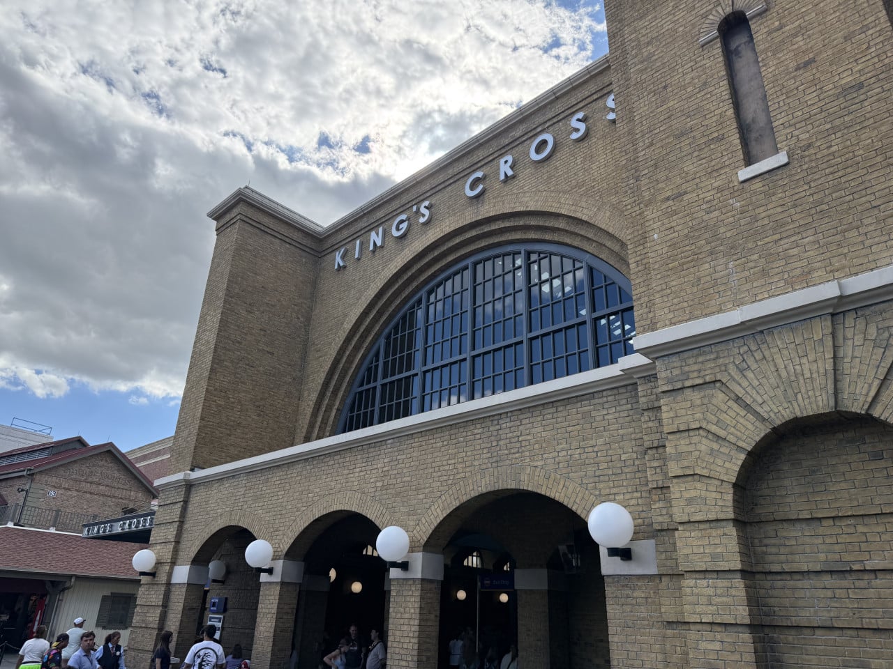 Budova King's Cross v Universal Studios Orlando s návštěvníky před vchodem a oblačnou oblohou.